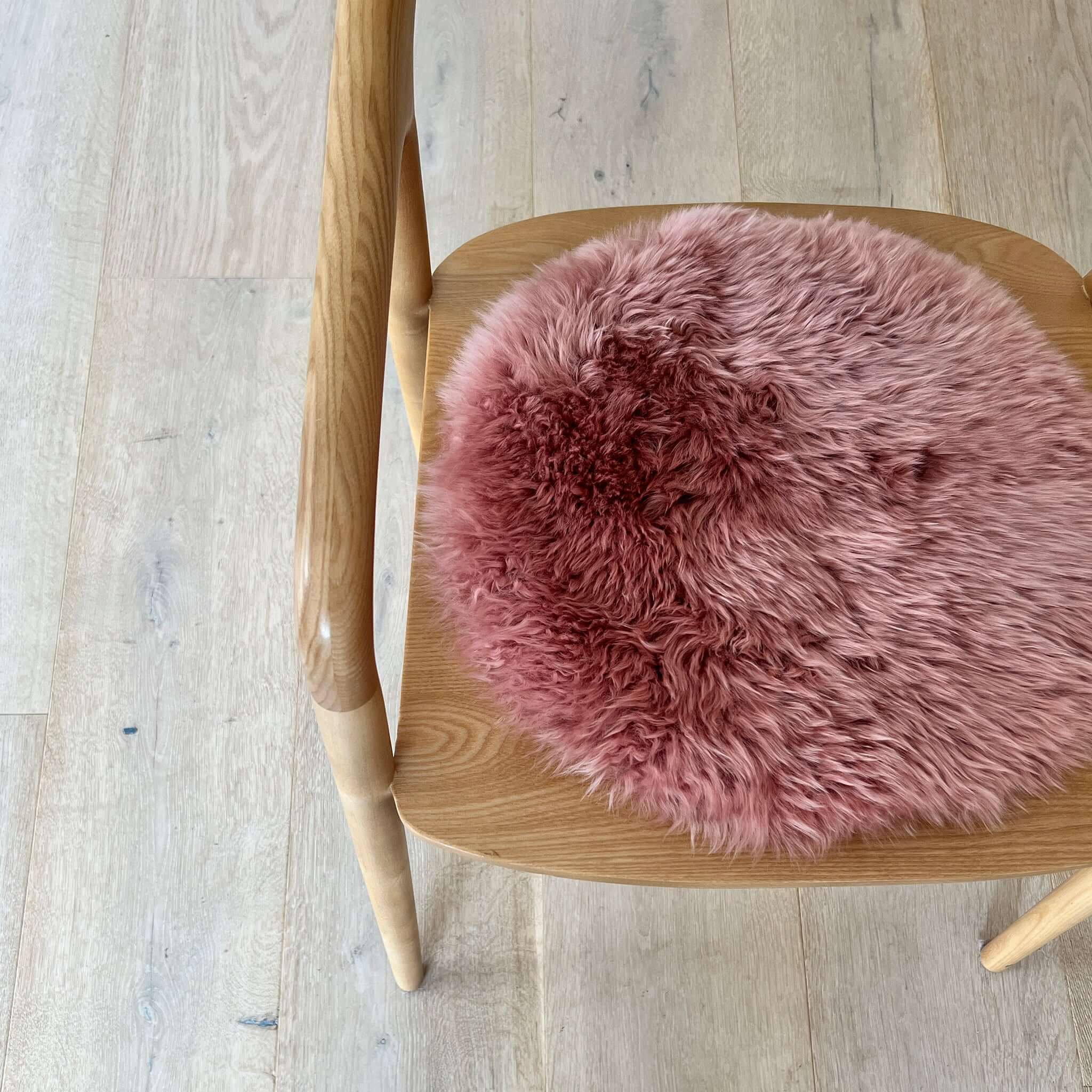 Alt Tag: Long Wool Sheepskin Circle Chair Pad - Dark Rose on wooden chair, plush round one-sided sheepskin seat pad
