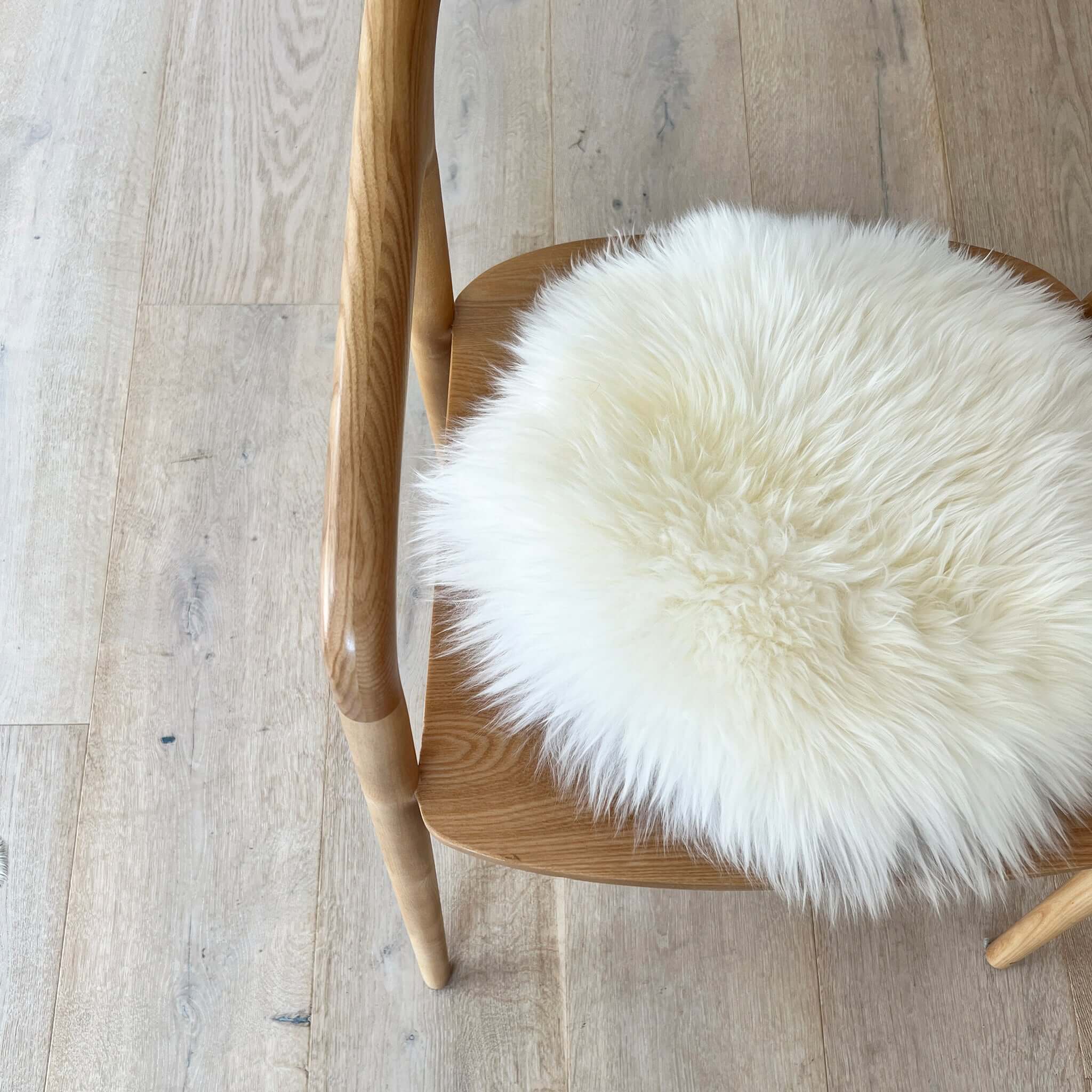 Alt Tag: Long Wool Sheepskin Circle Chair Pad - Ivory on wooden chair, fluffy one-sided 37cm round sheepskin seat pad