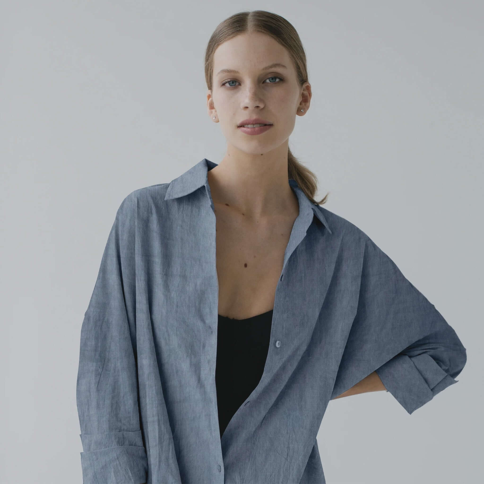 Woman wearing a blue oversized shirt against a plain background