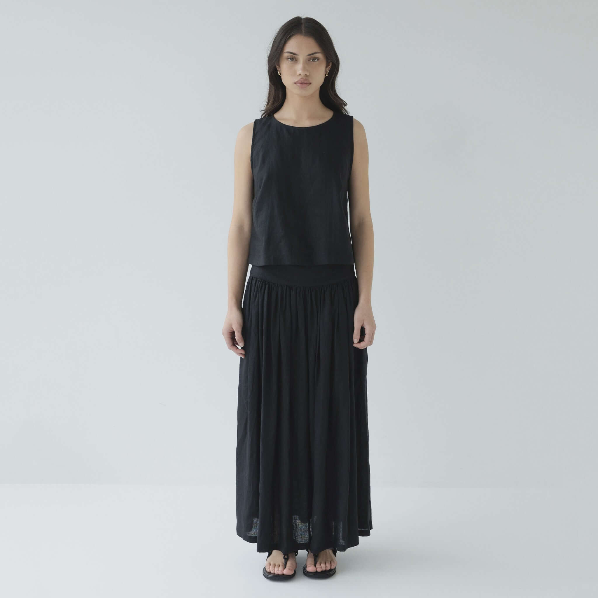 Woman wearing a black sleeveless top and long skirt on a white background