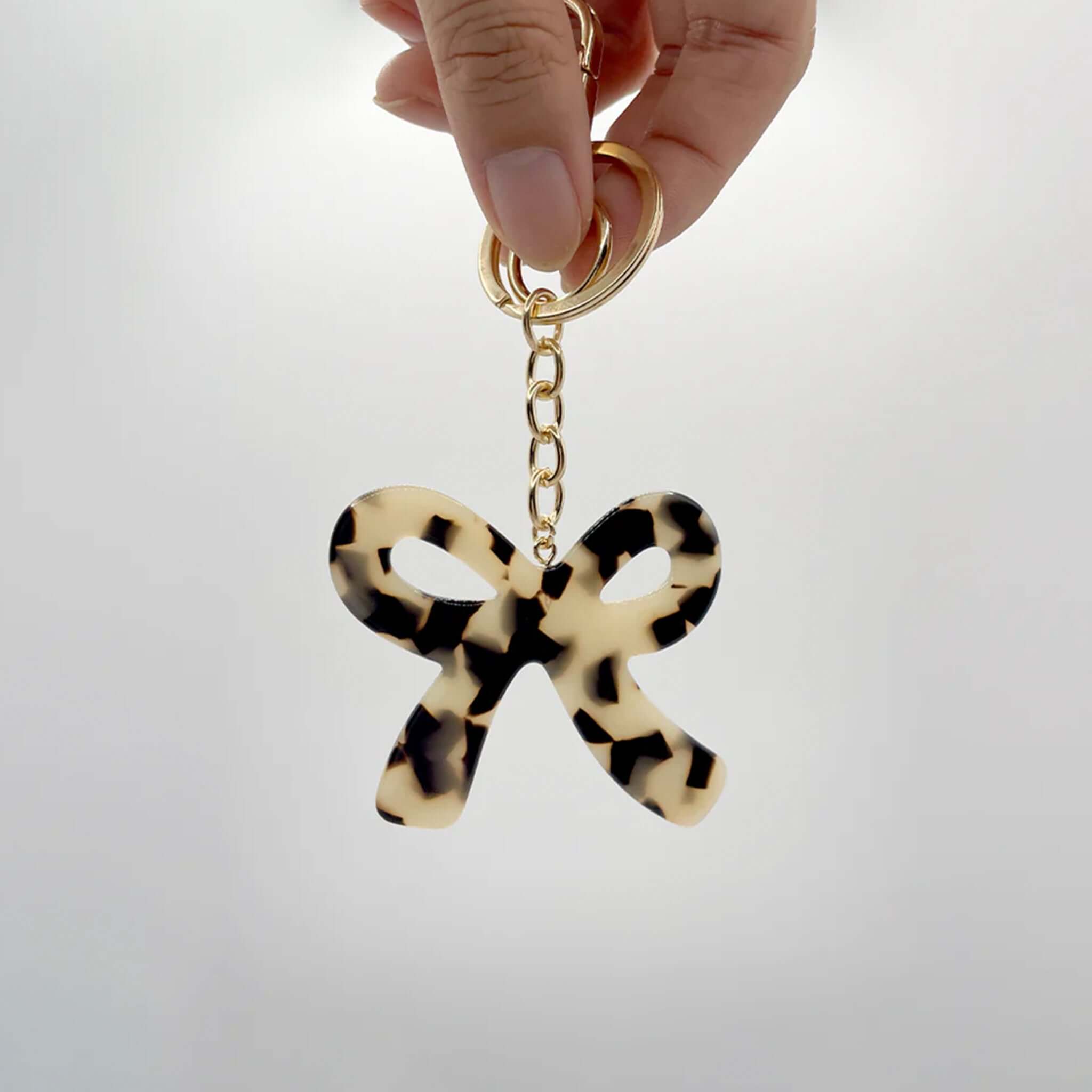 Alt Tag: Sophie Bow Beauty Keychain - Light Tort acetate tortoise bow keychain with gold hardware, held in hand