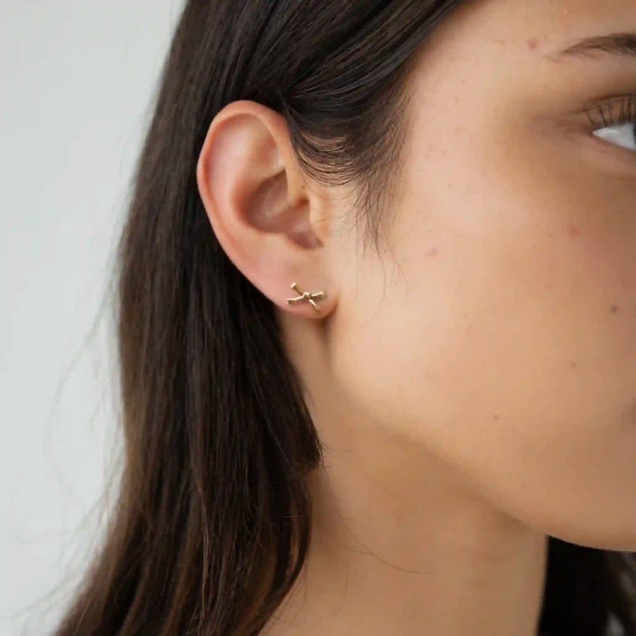 Close-up of an ear wearing a gold cross earring against a neutral background