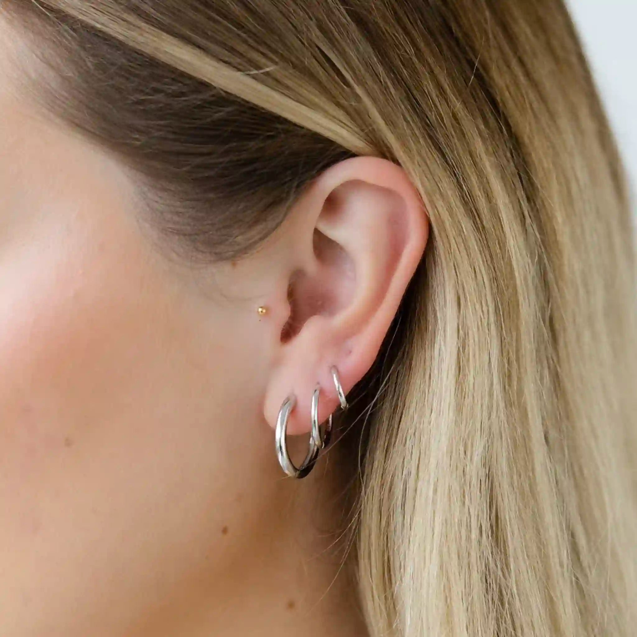 Close-up of an ear wearing two silver hoop earrings with blonde hair.