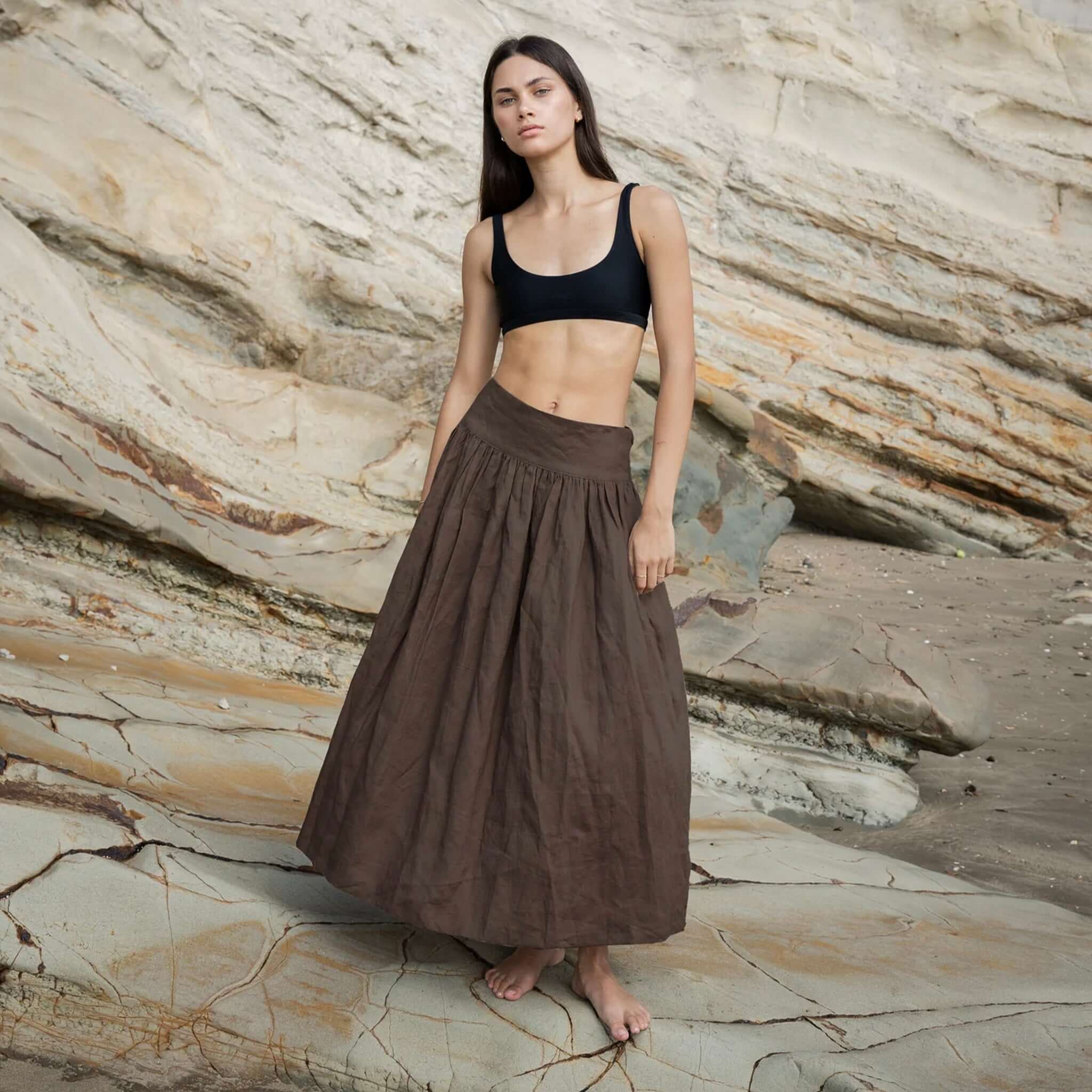 Alt Tag: Sophie I'm Ready Linen Skirt - Cocoa full-length gathered linen skirt with wide waistband, side pockets, worn outdoors on rocky beach