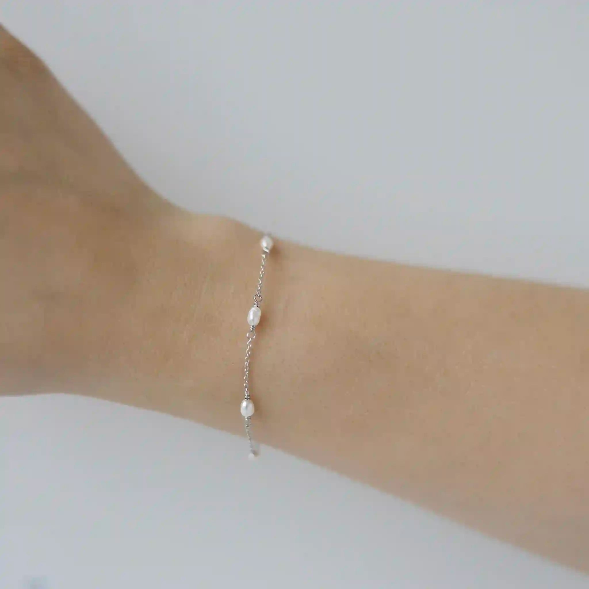 Silver bracelet with pearls on a wrist against a white background