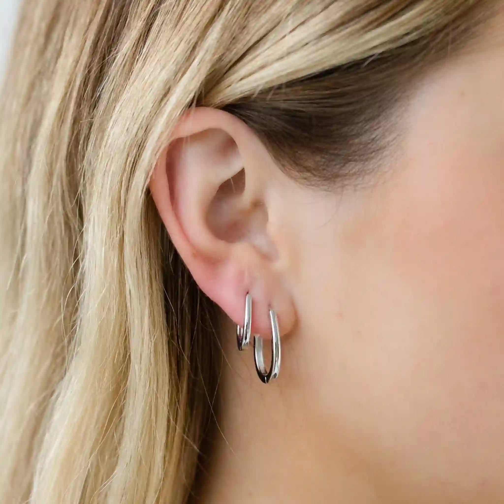 Close-up of a person wearing silver hoop earrings with blonde hair.