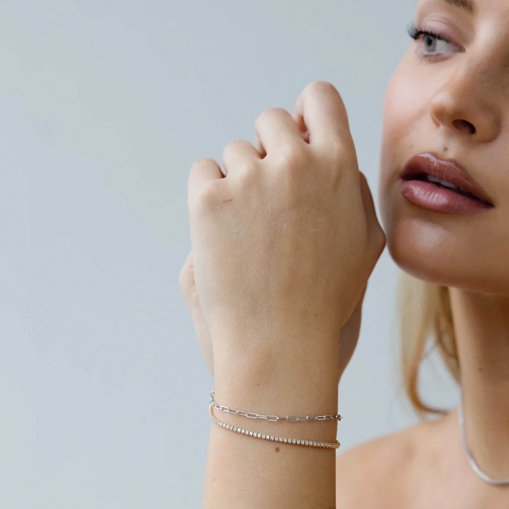 Close-up of a woman's hand wearing a gold bracelet on a plain background