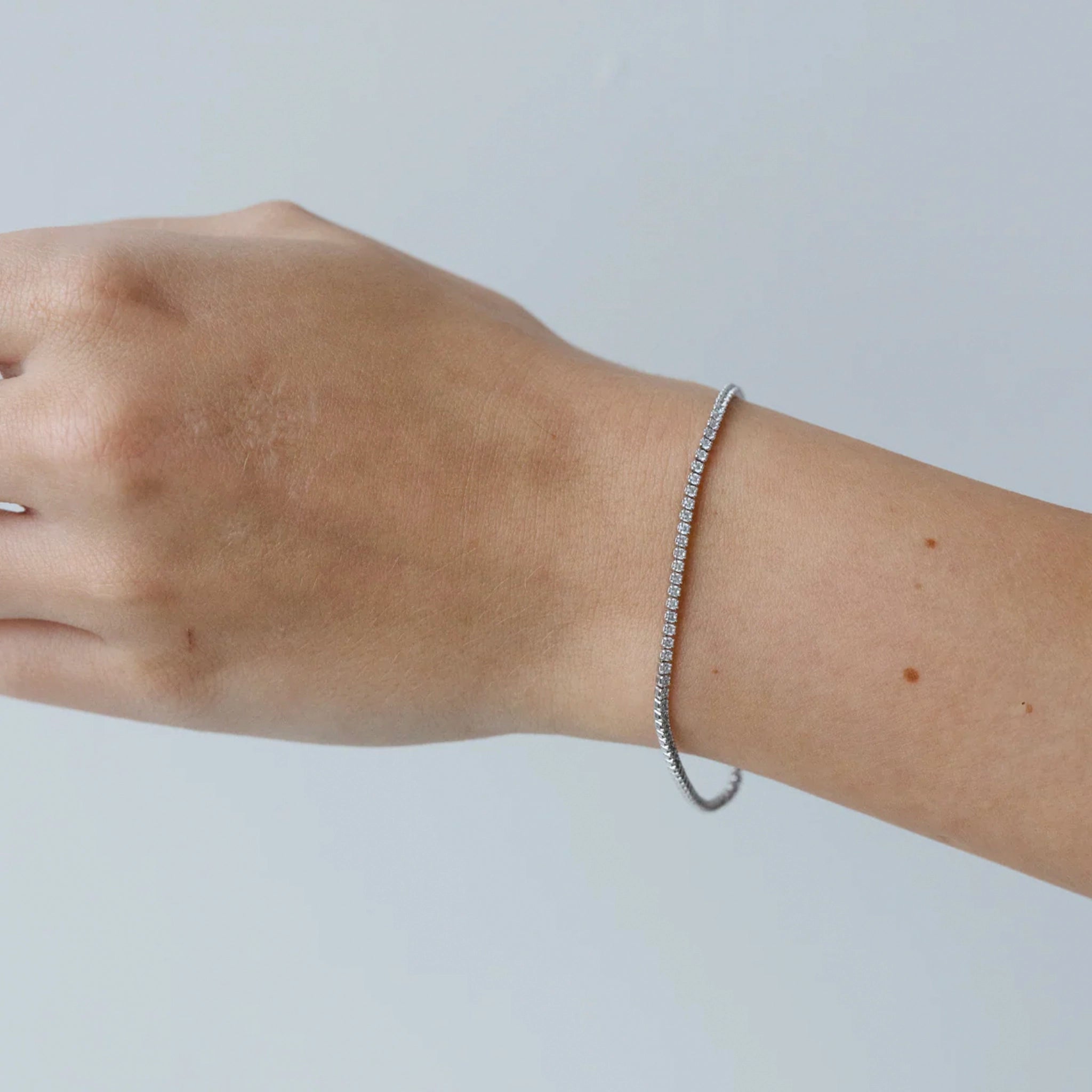 Silver bracelet on a wrist against a plain background