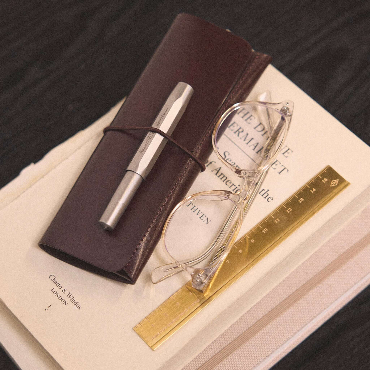 Milligram Recycled Leather Pen Case - Chocolate on a table with glasses and a ruler.