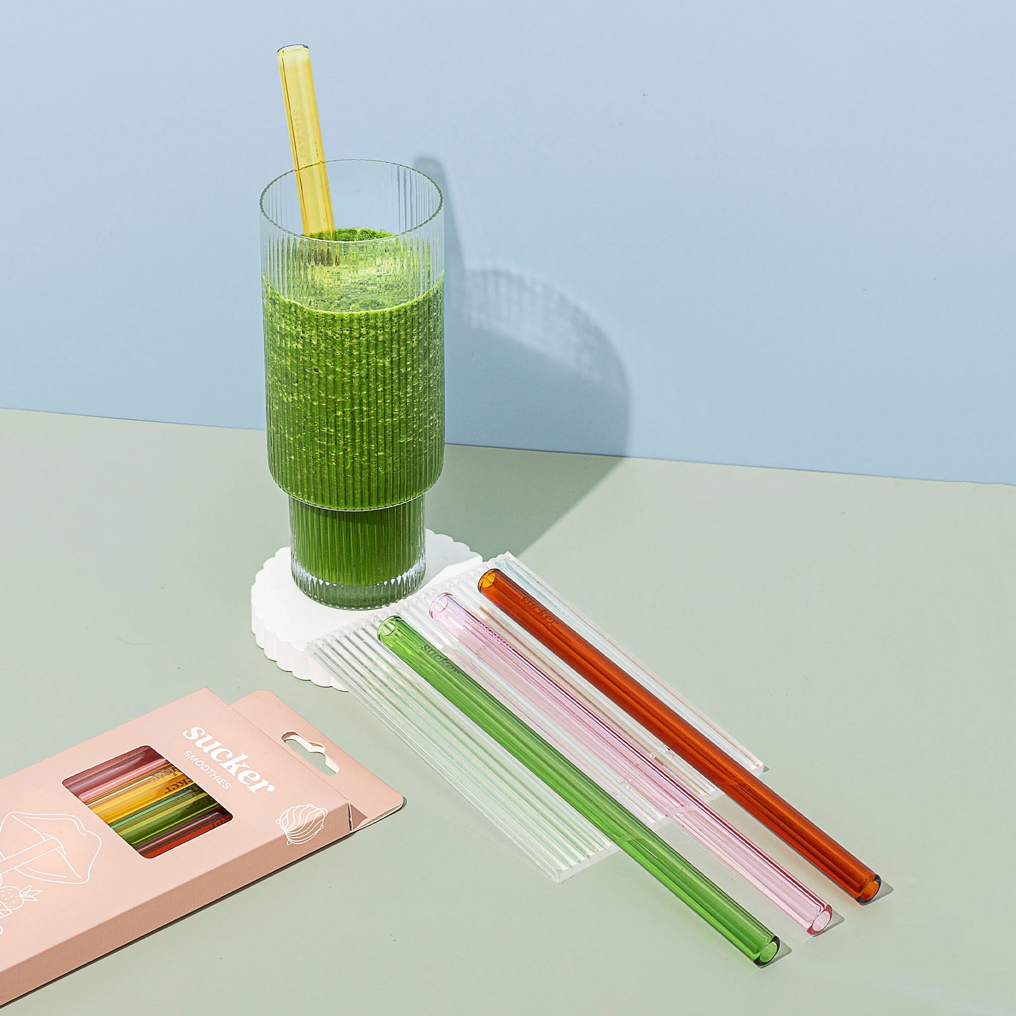 Set of colorful straws with a glass of green smoothie on a light surface.