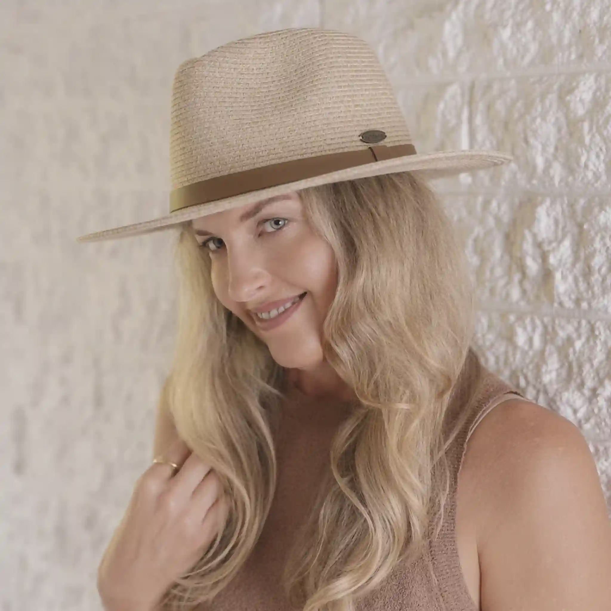 Woman wearing a straw hat with a brown band against a textured wall.