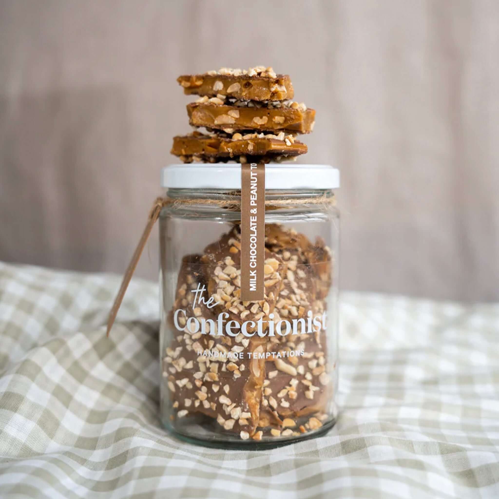 Alt Tag: The Confectionist Milk Chocolate Peanut Toffee - Small in glass jar, handcrafted buttery toffee with roasted peanuts coated in milk chocolate