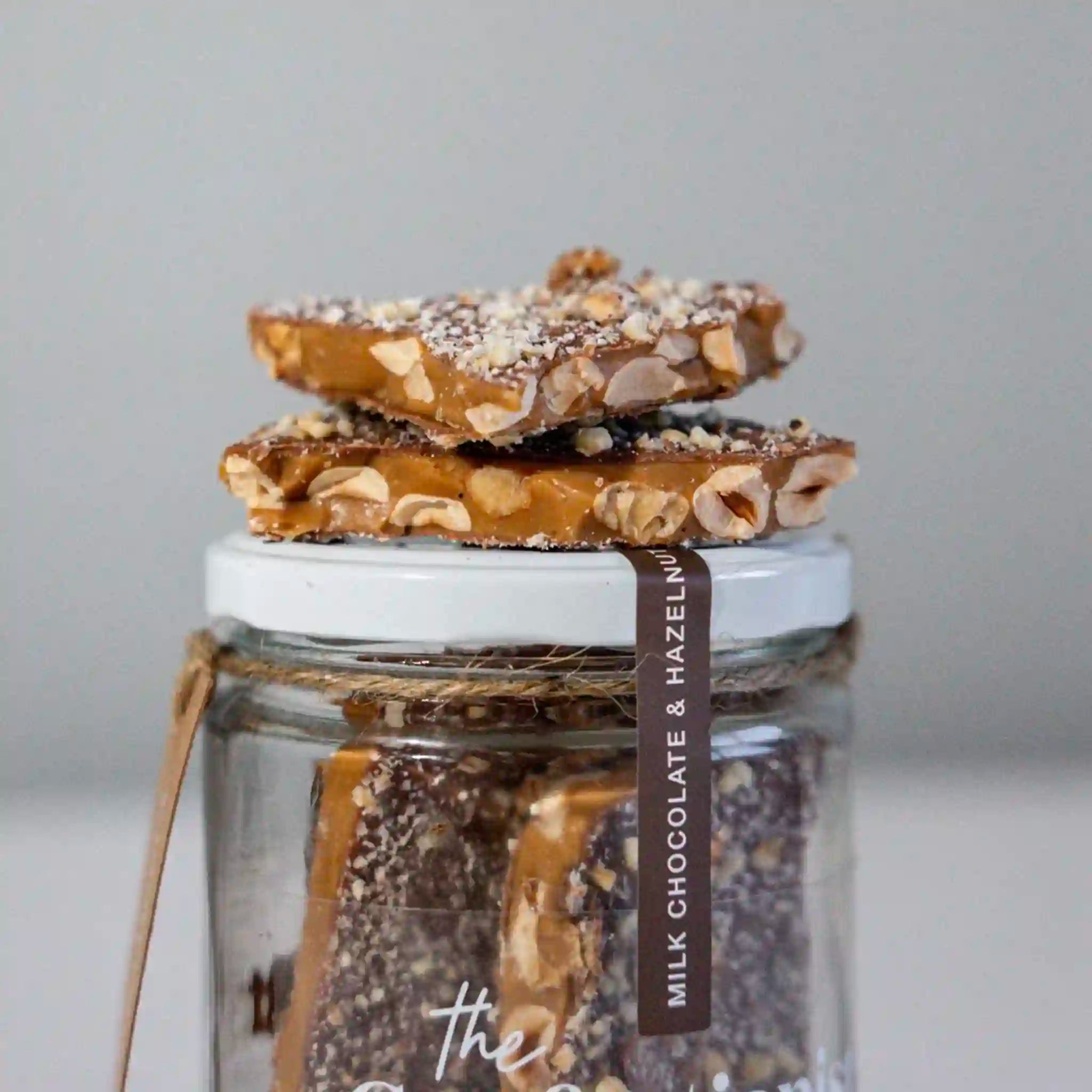 Jar of milk chocolate and hazelnut brittle with a label on a light gray background