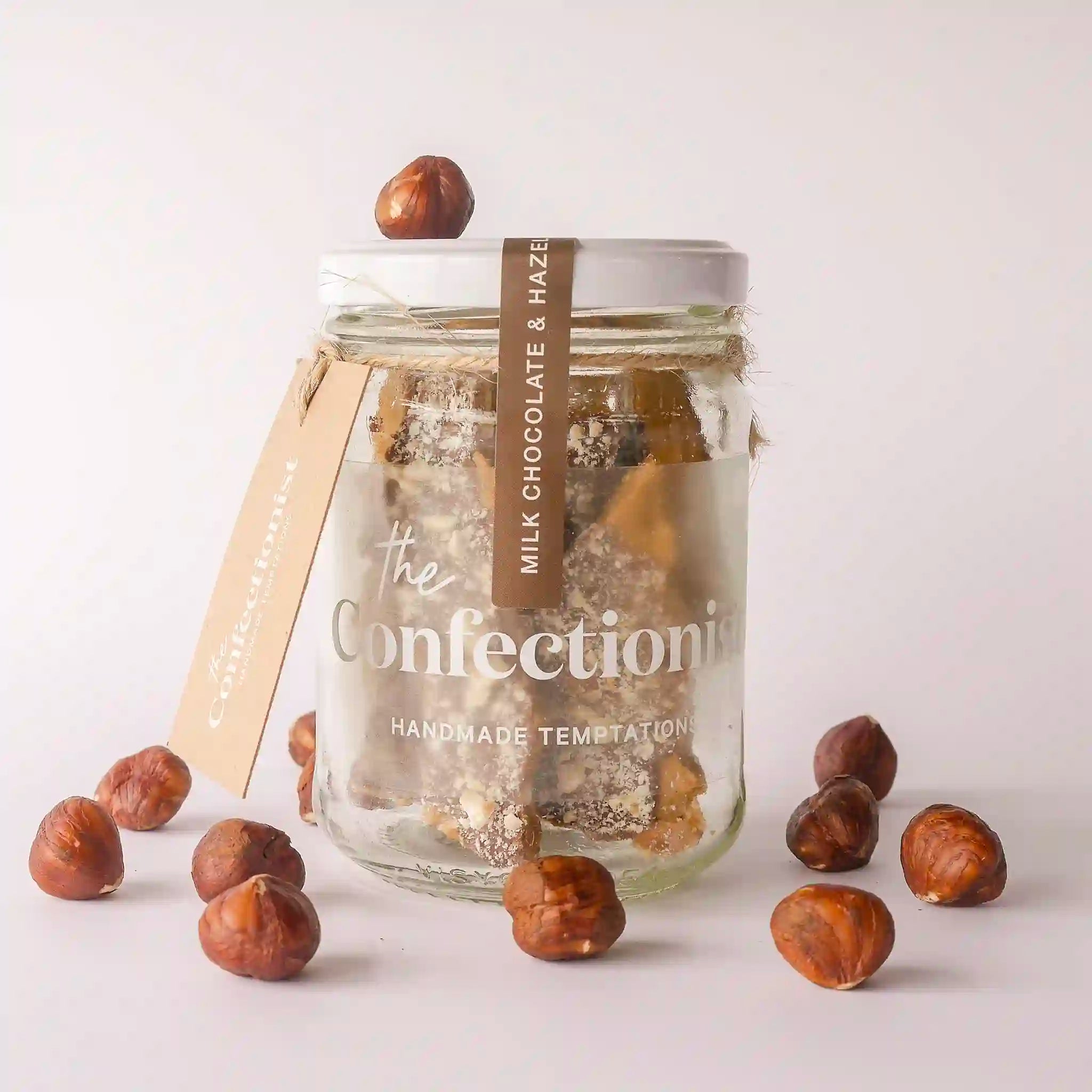 Glass jar with chocolate and hazelnuts labeled 'The Confectionery' on a light background