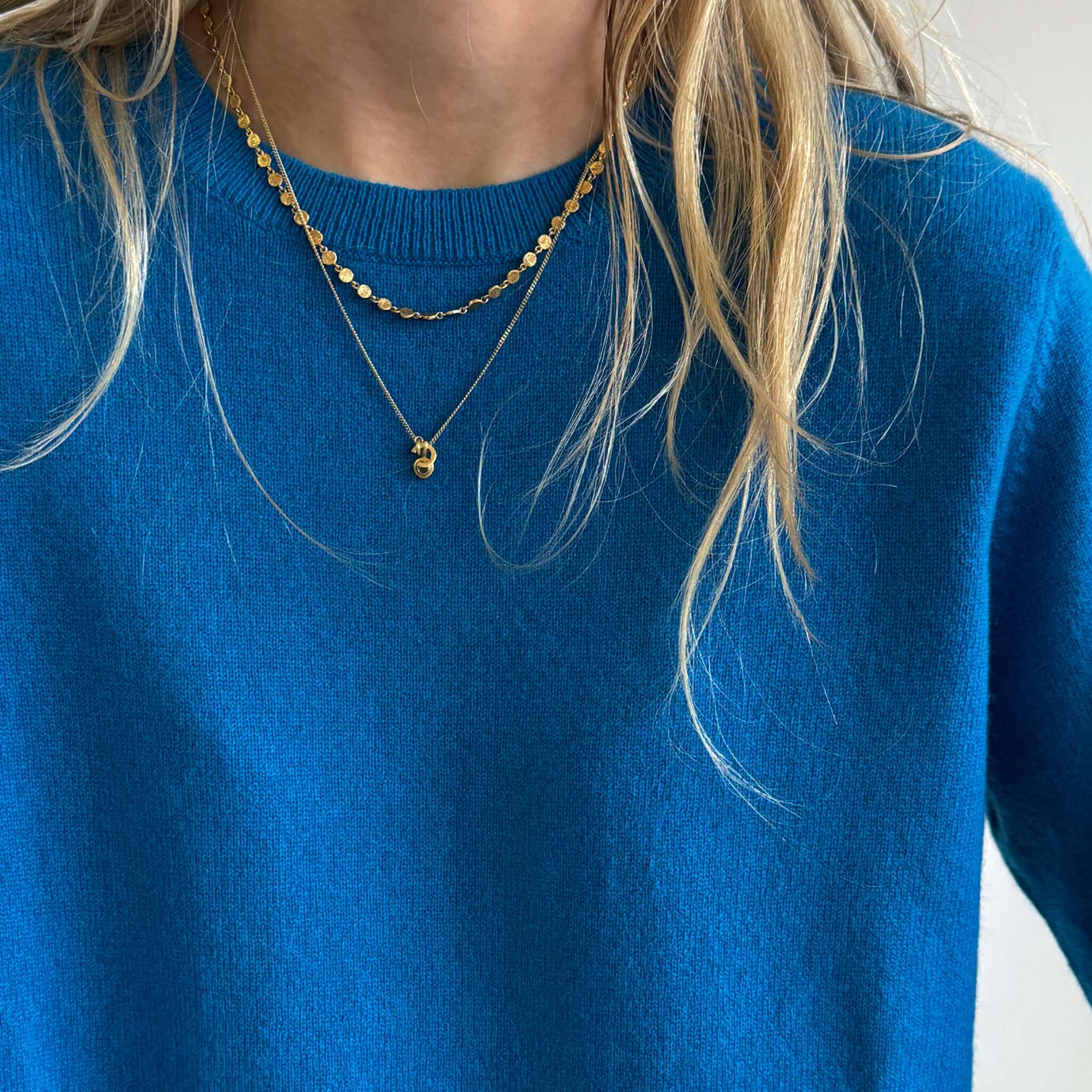 The Uniform Cashmere Crew Neck Sweater - Sapphire modeled with delicate gold necklaces.