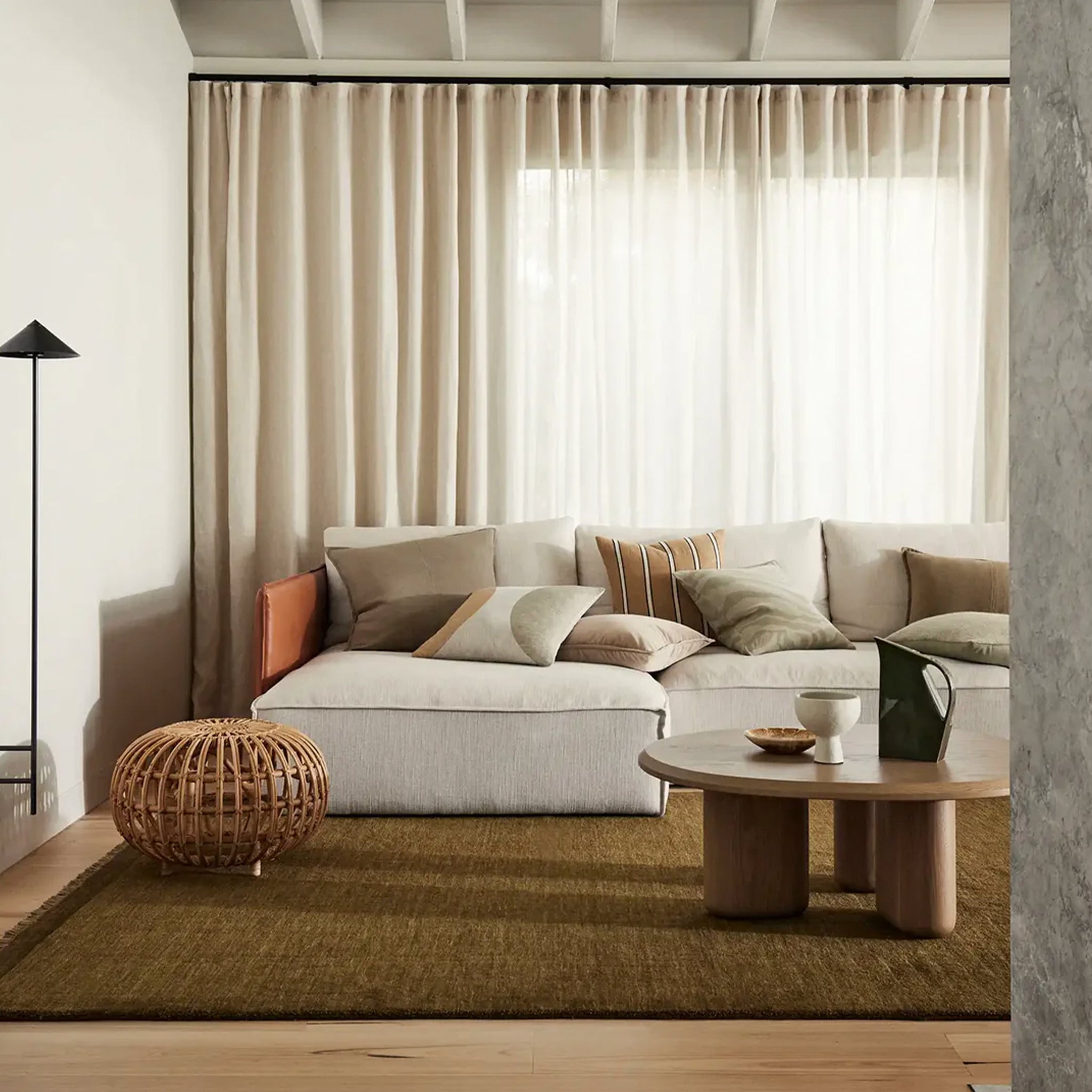 A contemporary gray rug with micro fringe and border detail, placed in a living room setting under a window with white curtains.