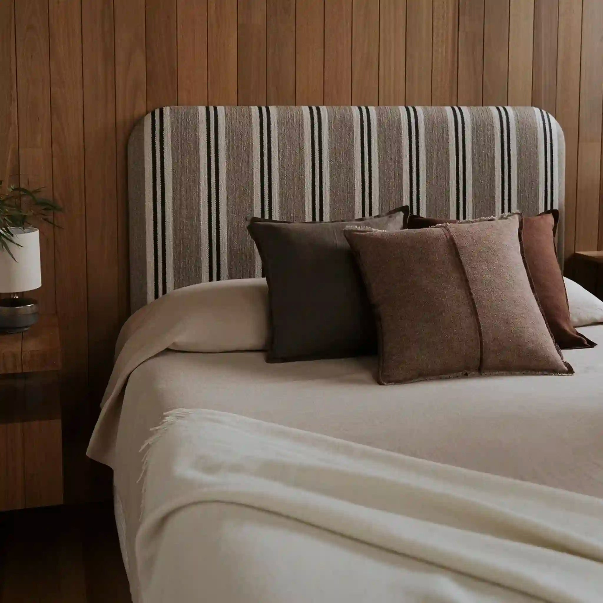 Bed with striped headboard and brown cushions in a bedroom setting.