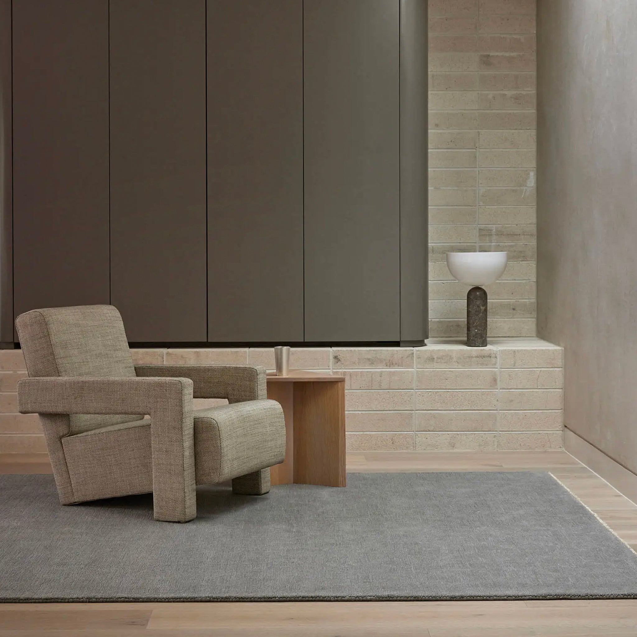 Beige armchair in a modern room with gray rug and wooden side table.