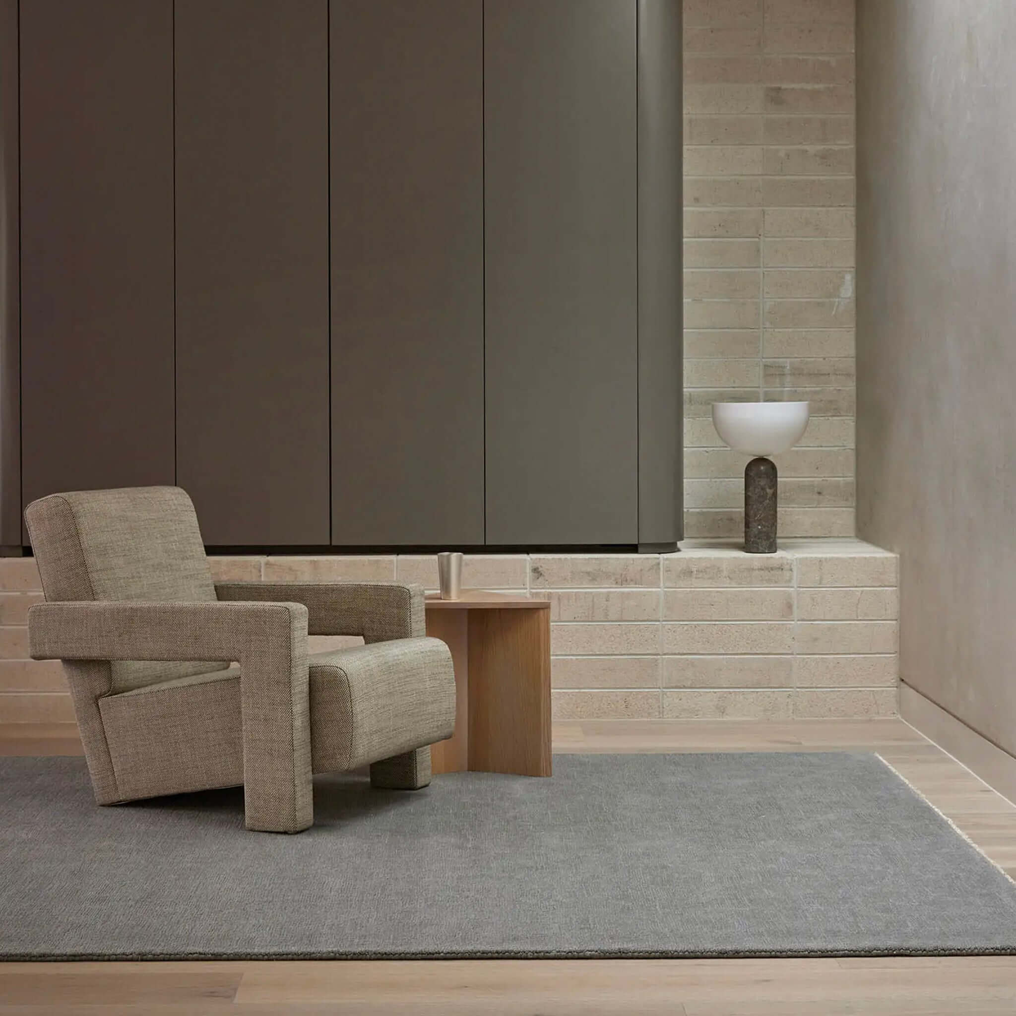 Beige armchair in a modern room with gray rug and wooden side table.