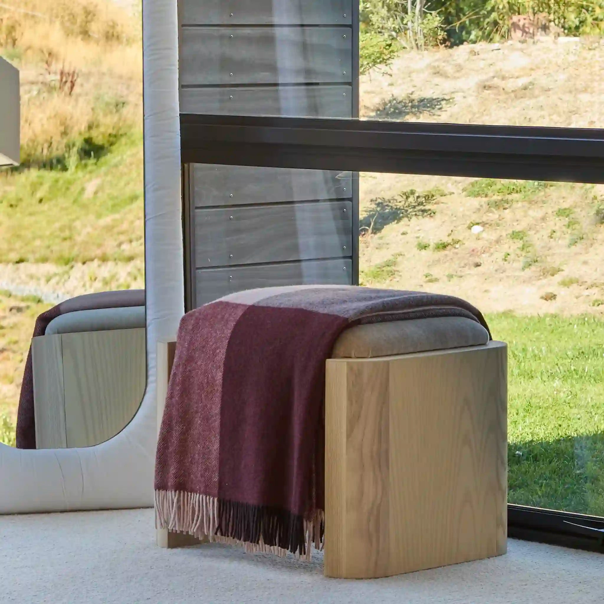 Wooden stool with a striped blanket draped over it, set against a scenic outdoor background.