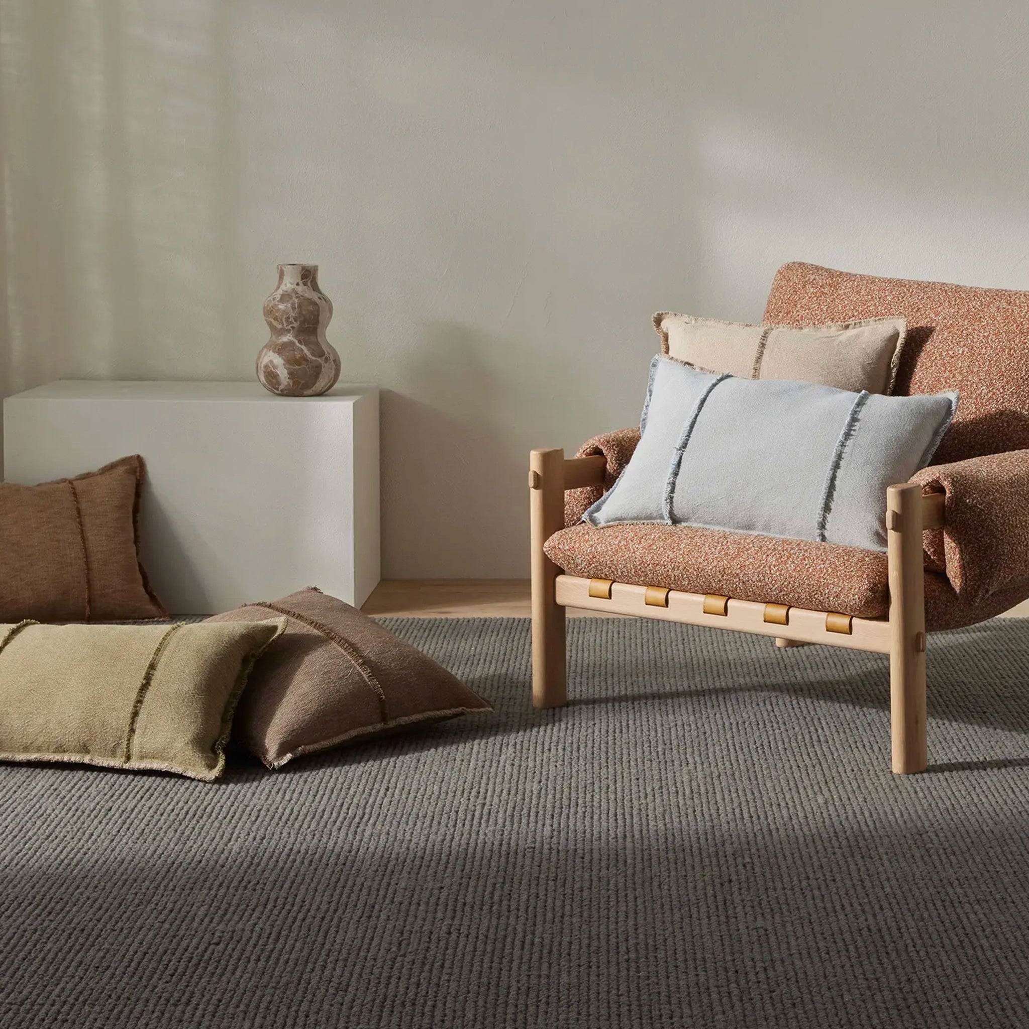 Modern living room with a brown armchair and cushions, a white side table, and a vase.
