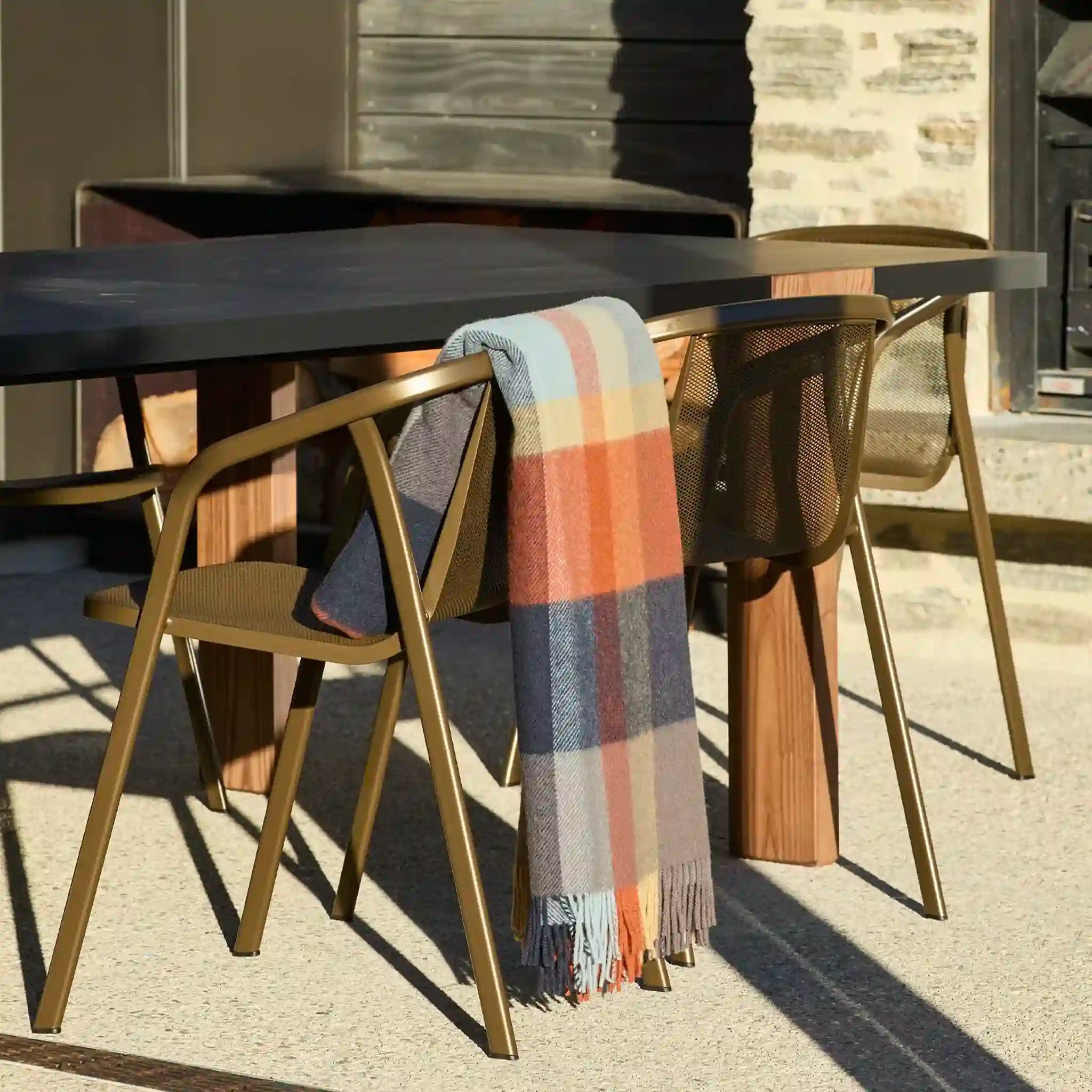 Outdoor setting with a wooden table and chairs, and a plaid blanket draped over one of the chairs.