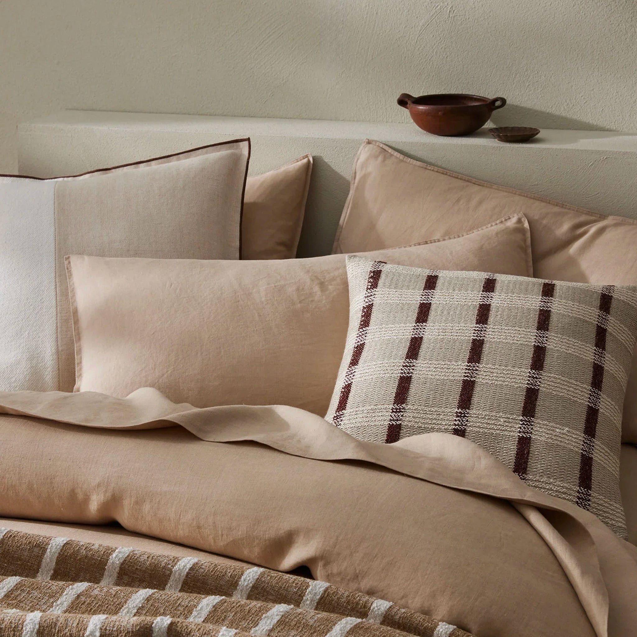 Neatly arranged pillows on a bed with a plaid throw blanket in a warm-toned room.