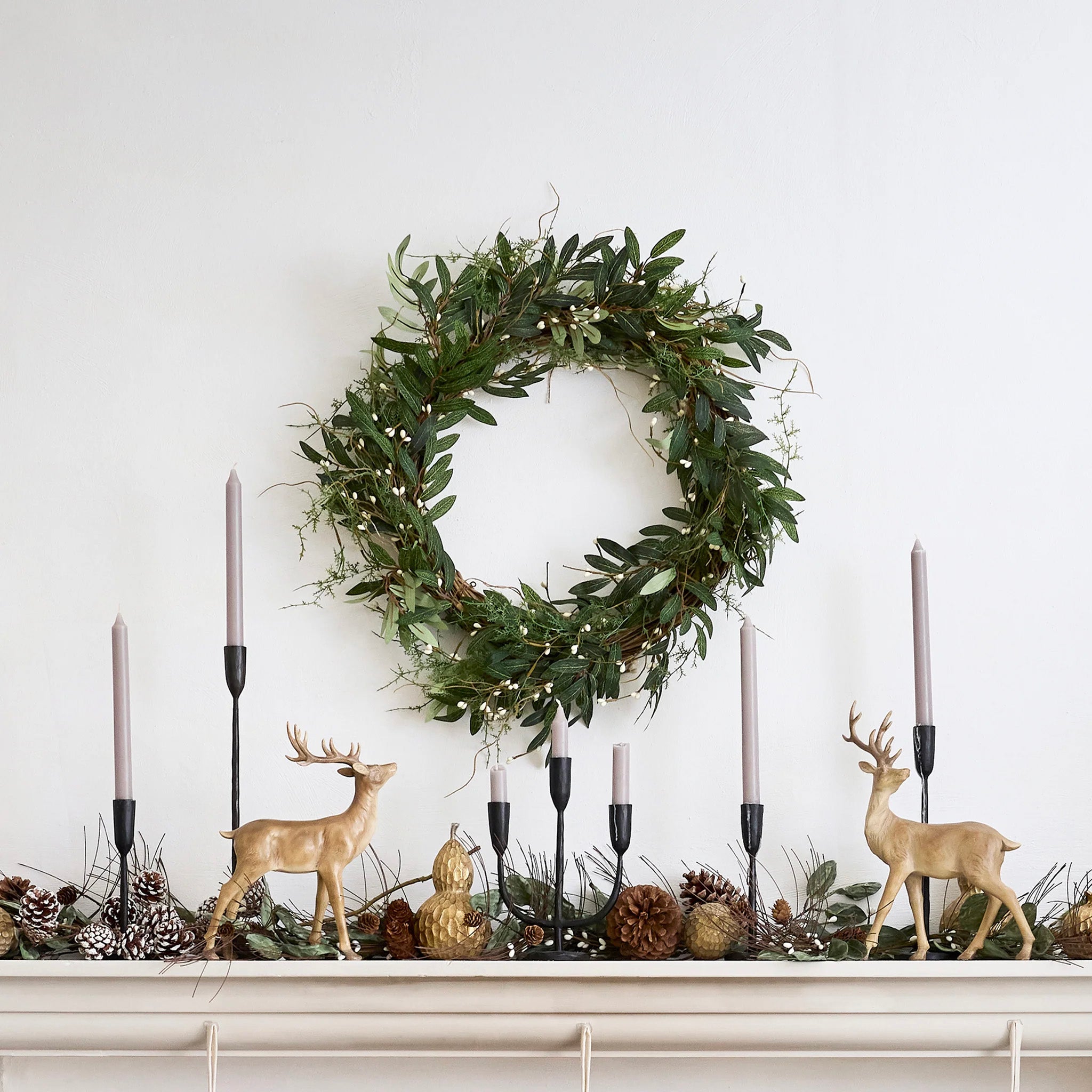A round wreath decoration with green pine branches, brown pinecones, and white berry flowers.