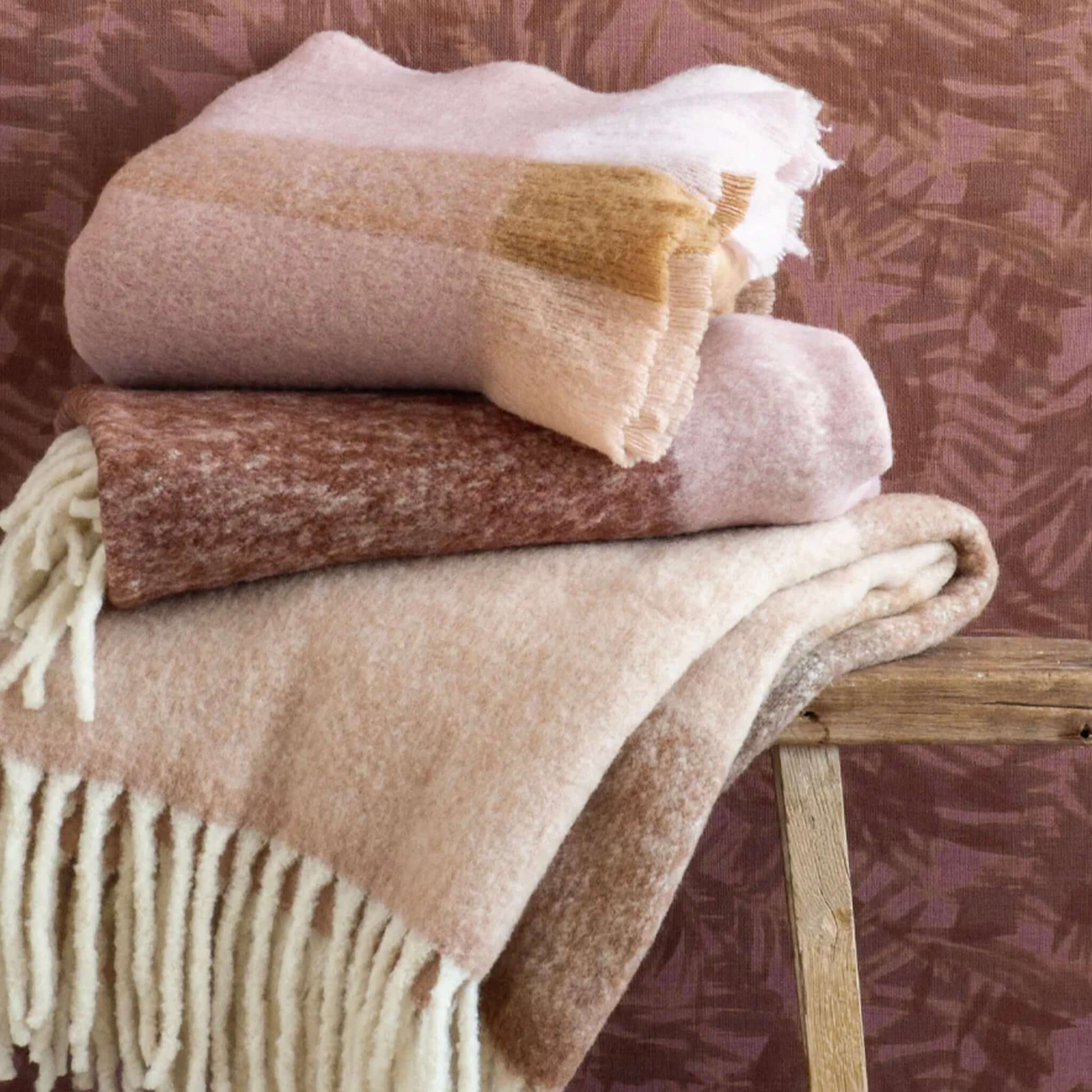 Bianca Lorenne Arundel Throw - Plum Blossom displayed with soft, brushed wool blankets and chunky tassels.