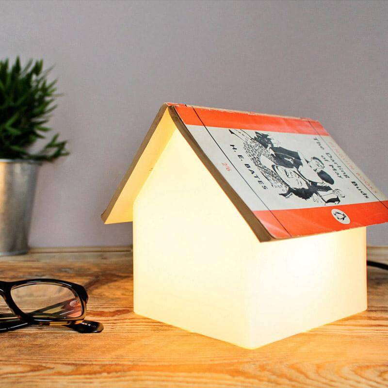A clear, frosted semi-transparent lamp designed to serve as a bookrest with a book on top, glowing with a warm light.