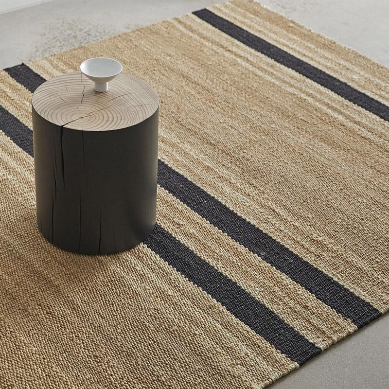 Beige striped rug with table on a concrete floor.