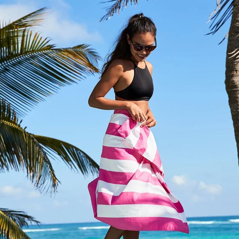 Woman on a beach wrapped in a pink striped beach towel.