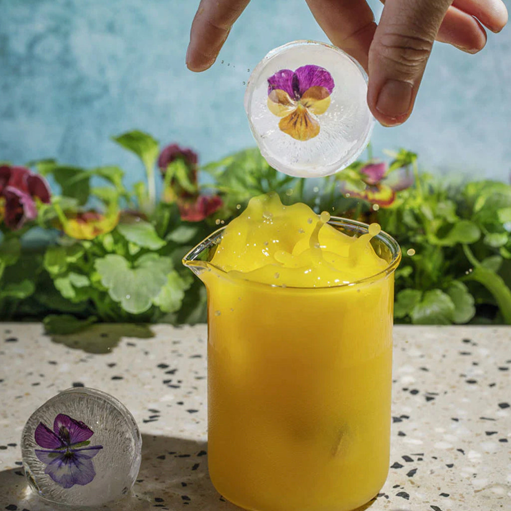 Round ice cube being dropped into an orange juice glass.