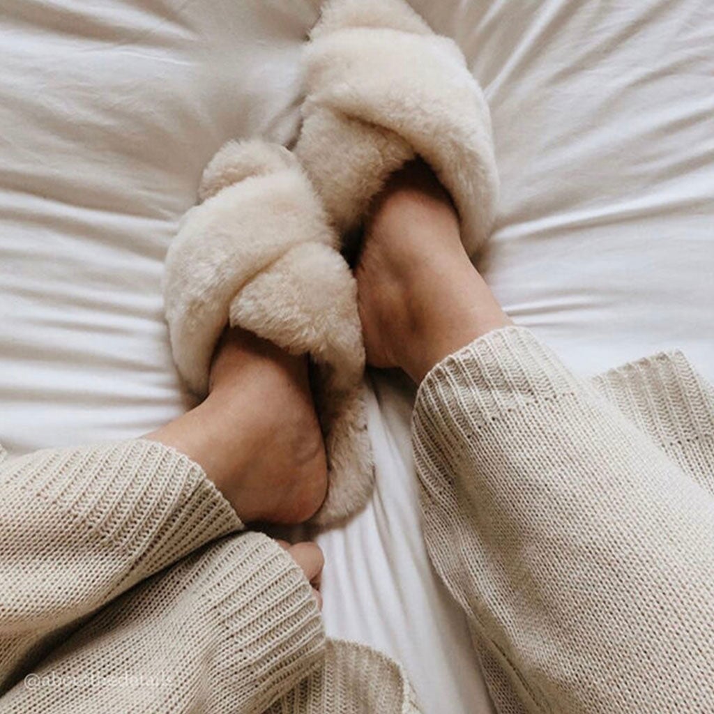 Alt Tag: EMU Mayberry Slippers - Natural fluffy sheepskin crossover strap open-toe slippers worn lounging on bed