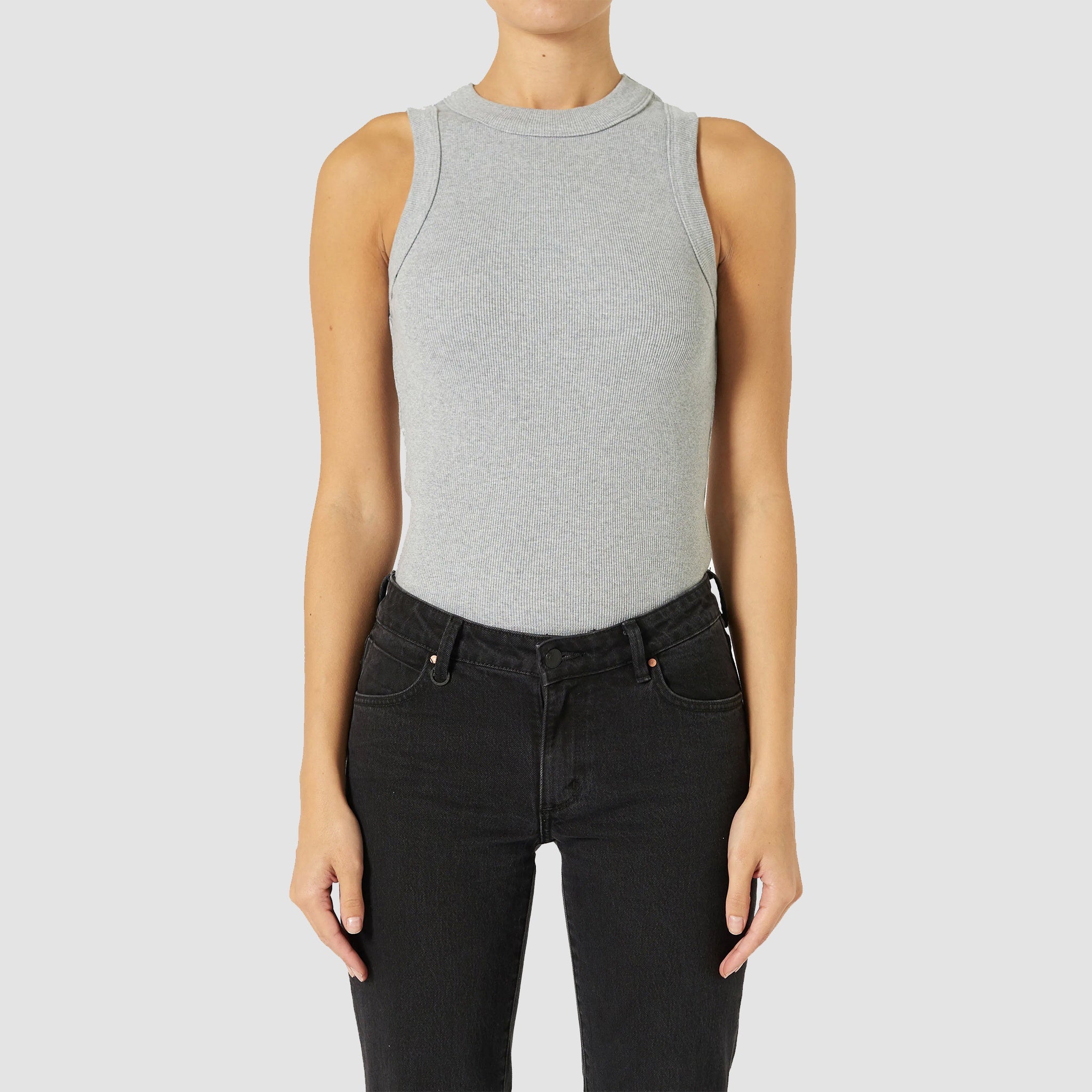 A female model wearing a grey marle tank top with wide rib binding on the hem and blue jeans.