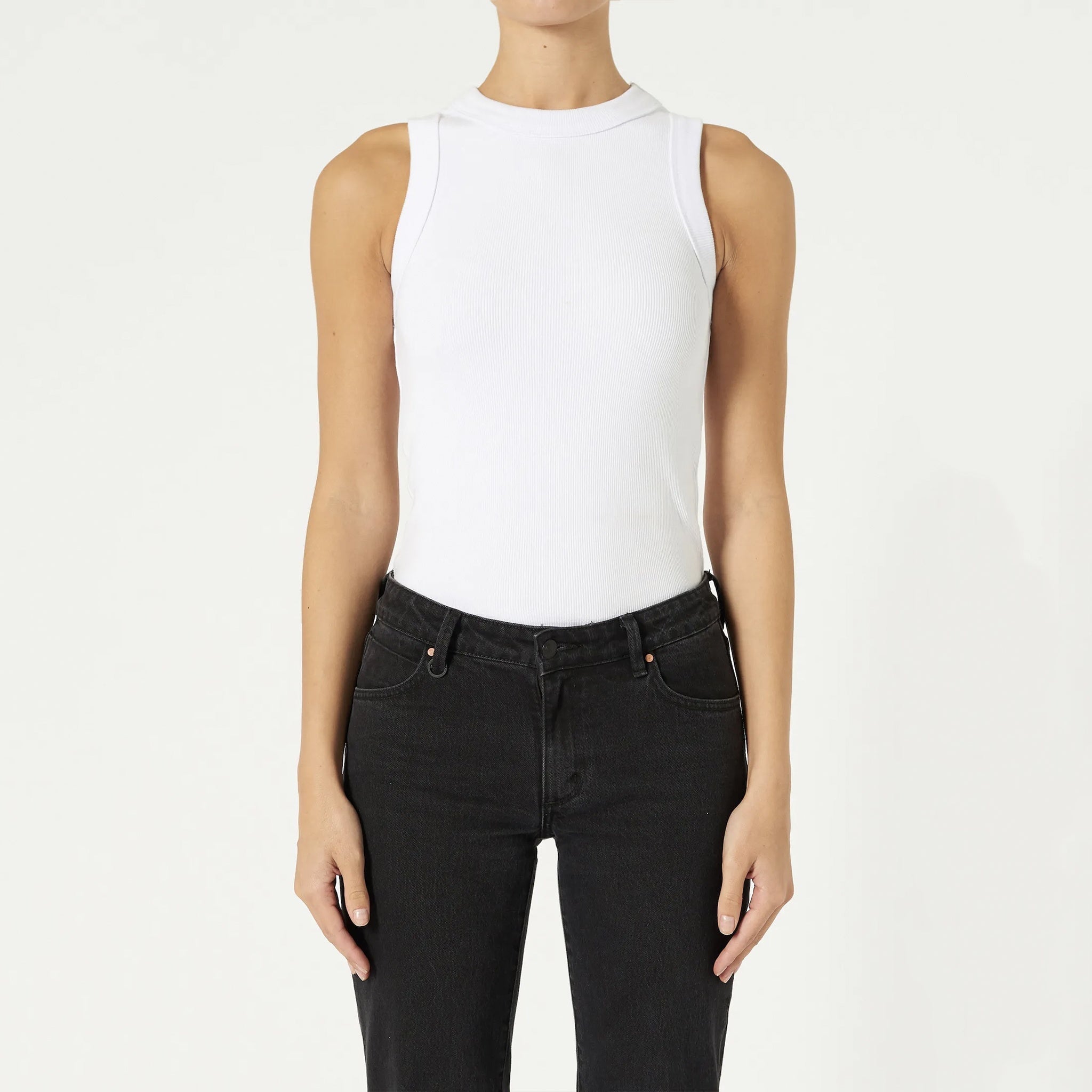 A person wearing a white singlet and  black jeans, standing against a white background.