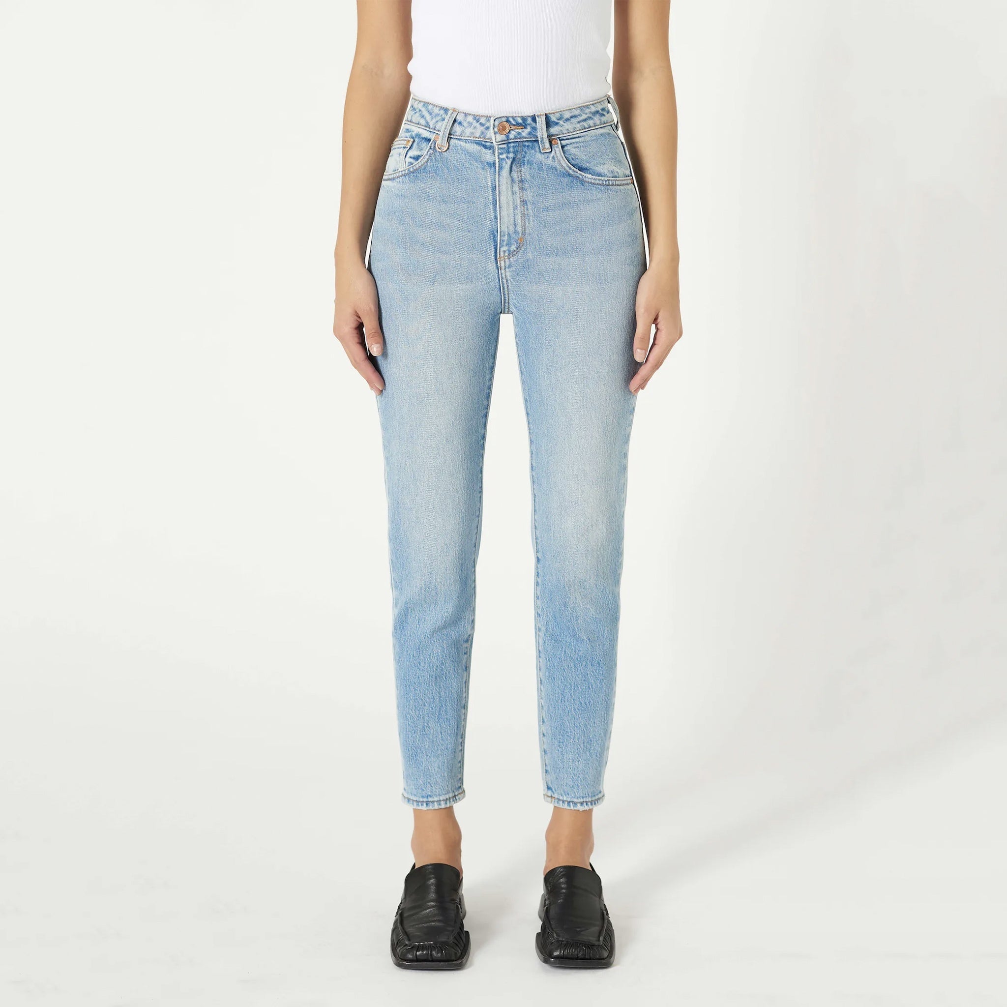 A person wearing a white strapless top and blue jeans, standing against a white background.