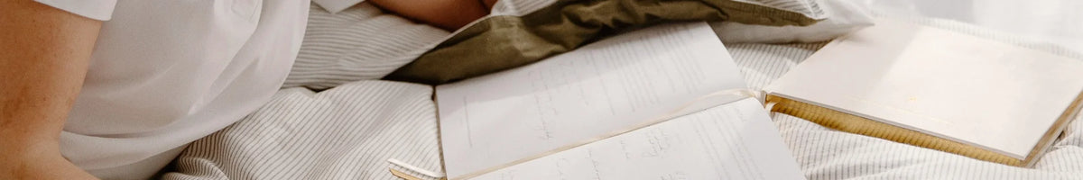 Olive + Page journals open on a bed with striped linen, brand header image