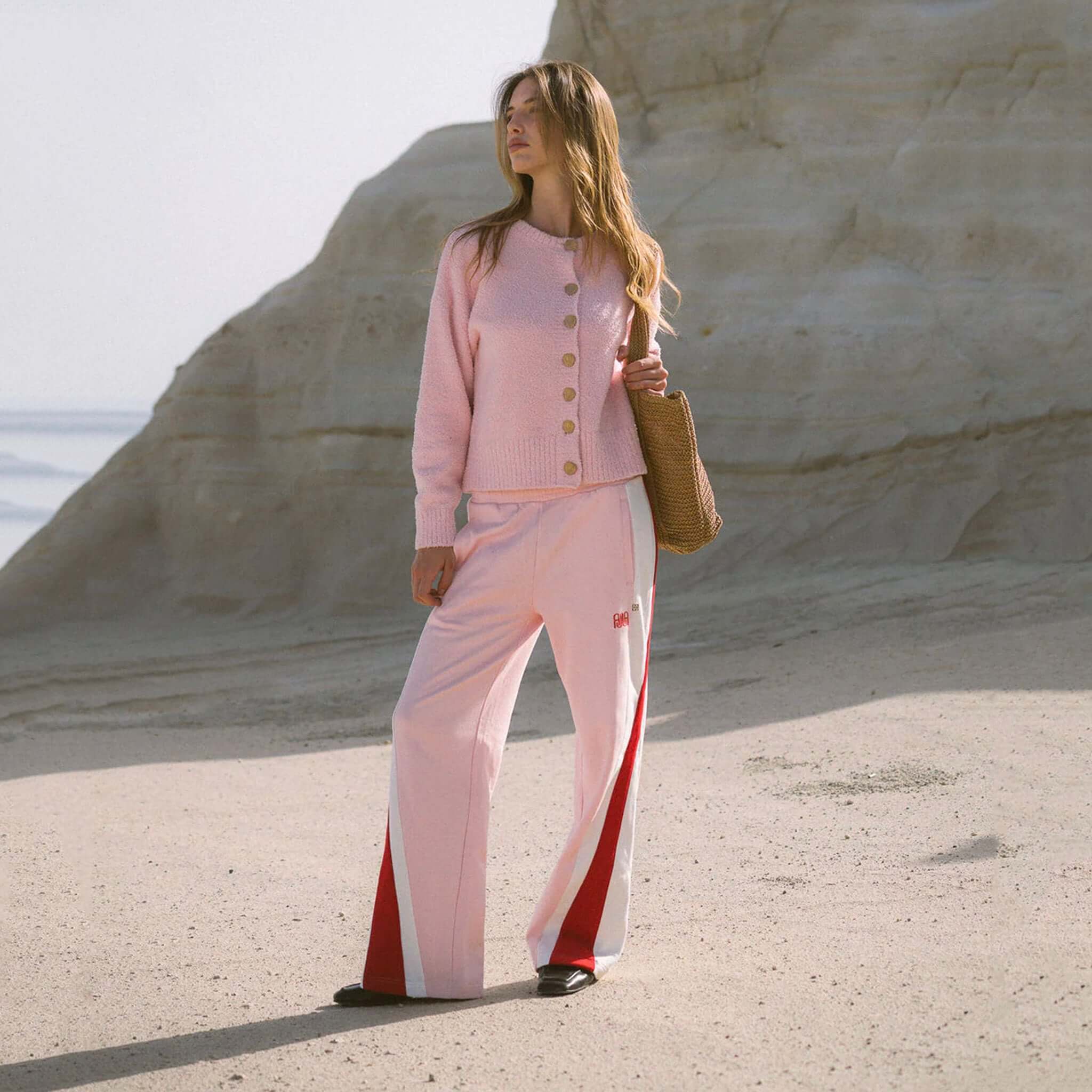 Woman wearing Araminta James Mallorca Trackpants - Ballet Pink and pink cardigan against a scenic backdrop.