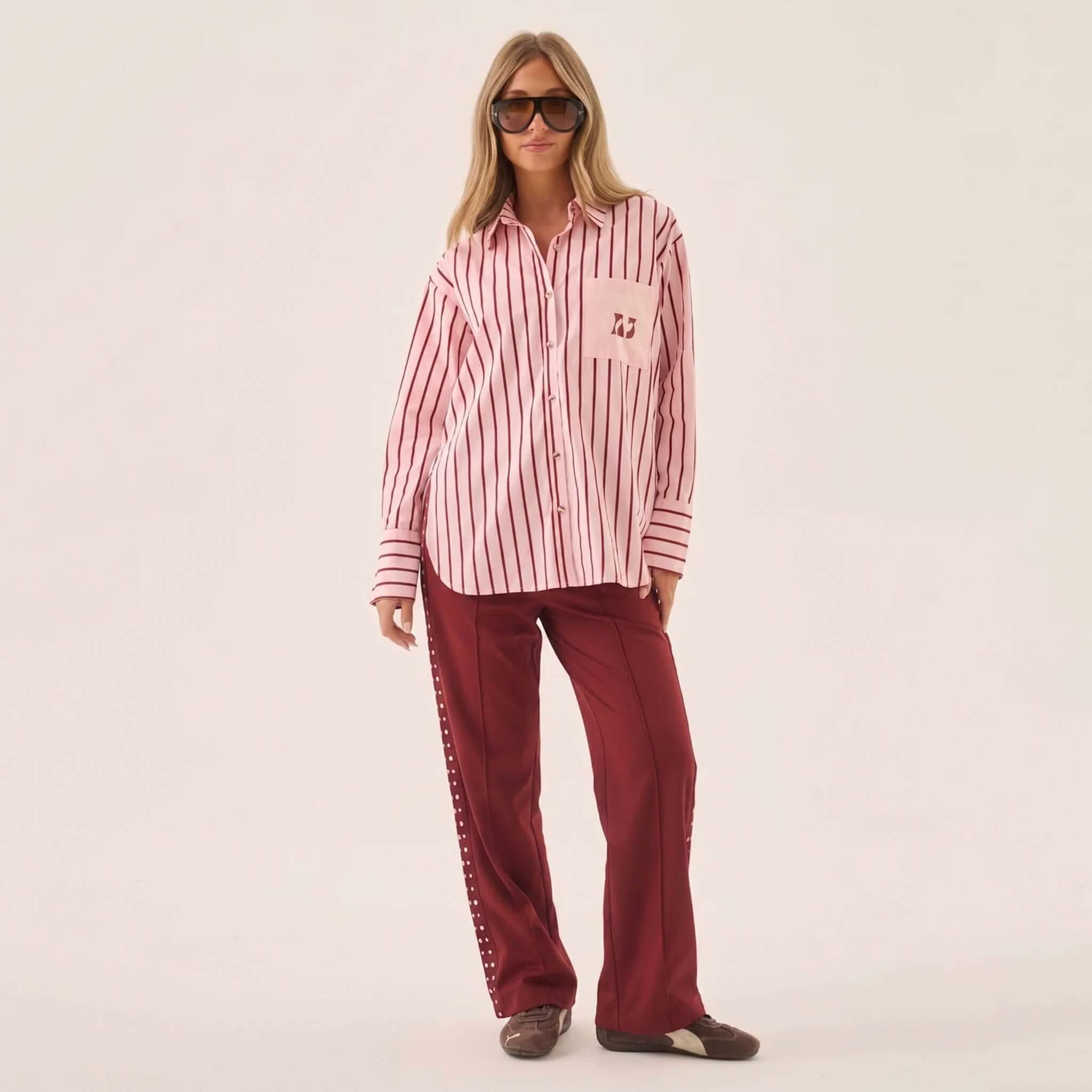 Woman wearing Araminta James Pomodoro Twill Pants - Burgundy with a striped pink shirt and sunglasses.