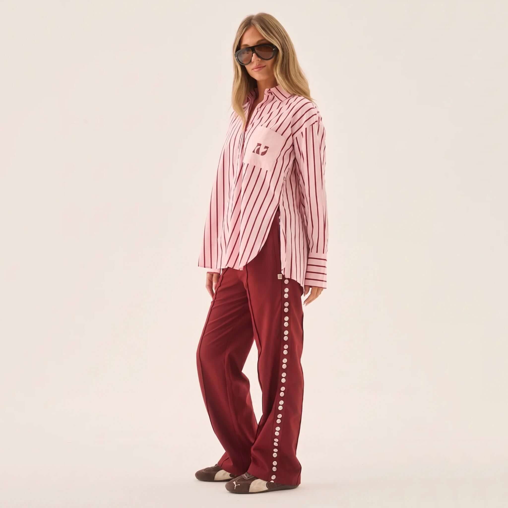 Araminta James Pomodoro Twill Pants - Burgundy styled with a striped shirt and oversized sunglasses.