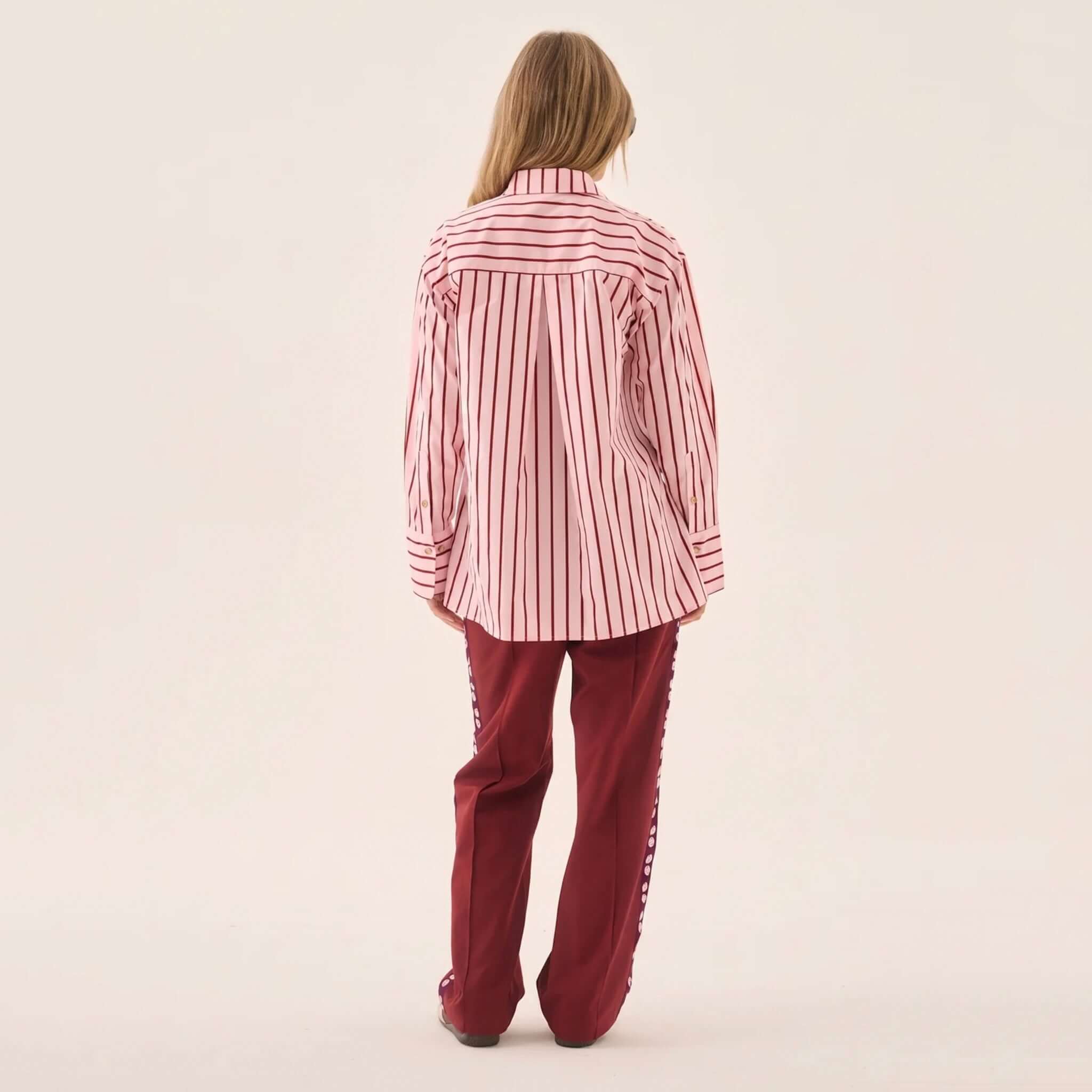 Model wearing Araminta James Pomodoro Twill Pants - Burgundy with a striped shirt from the back.
