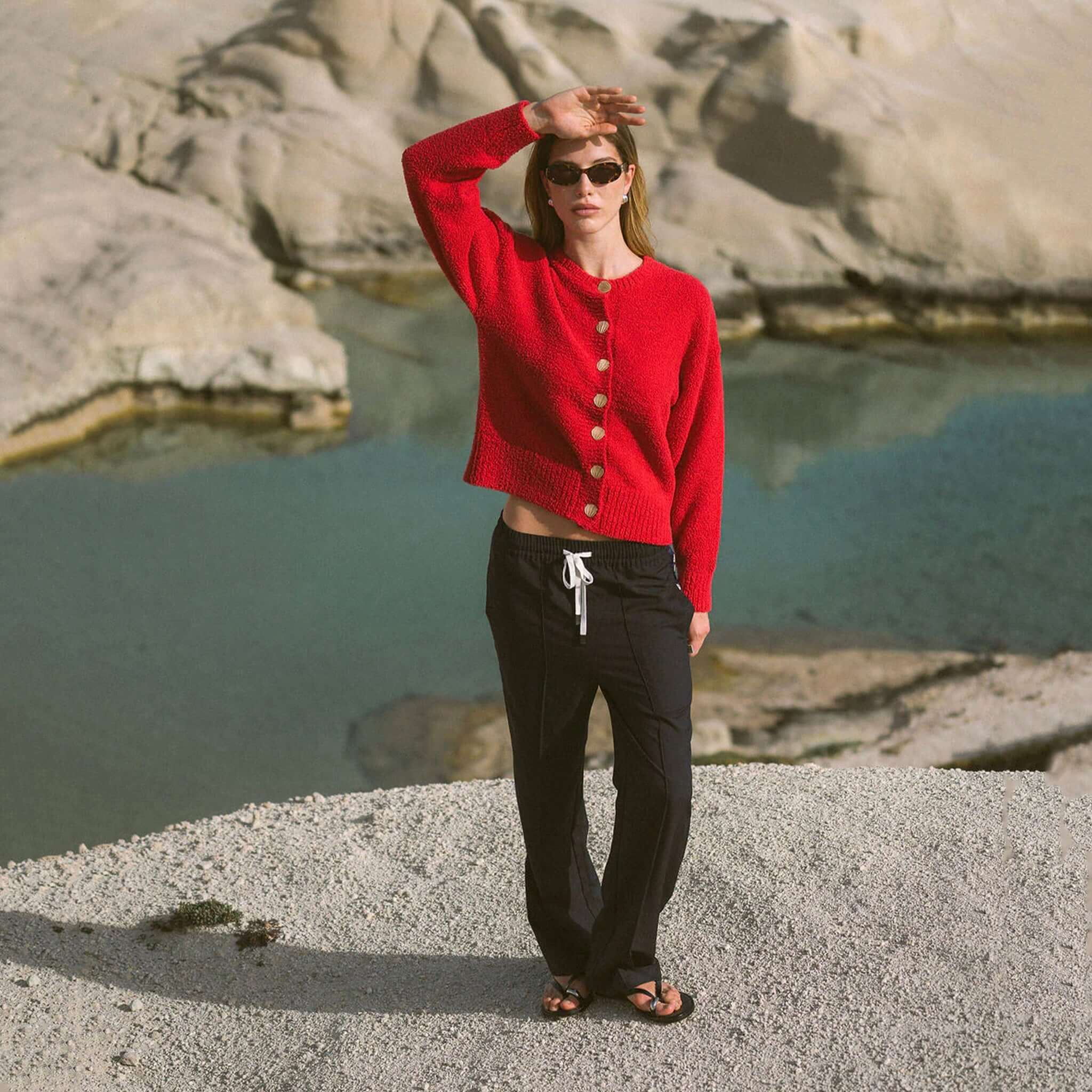 Woman wearing Araminta James Pomodoro Twill Pants - Midnight Navy with a red cardigan by water.