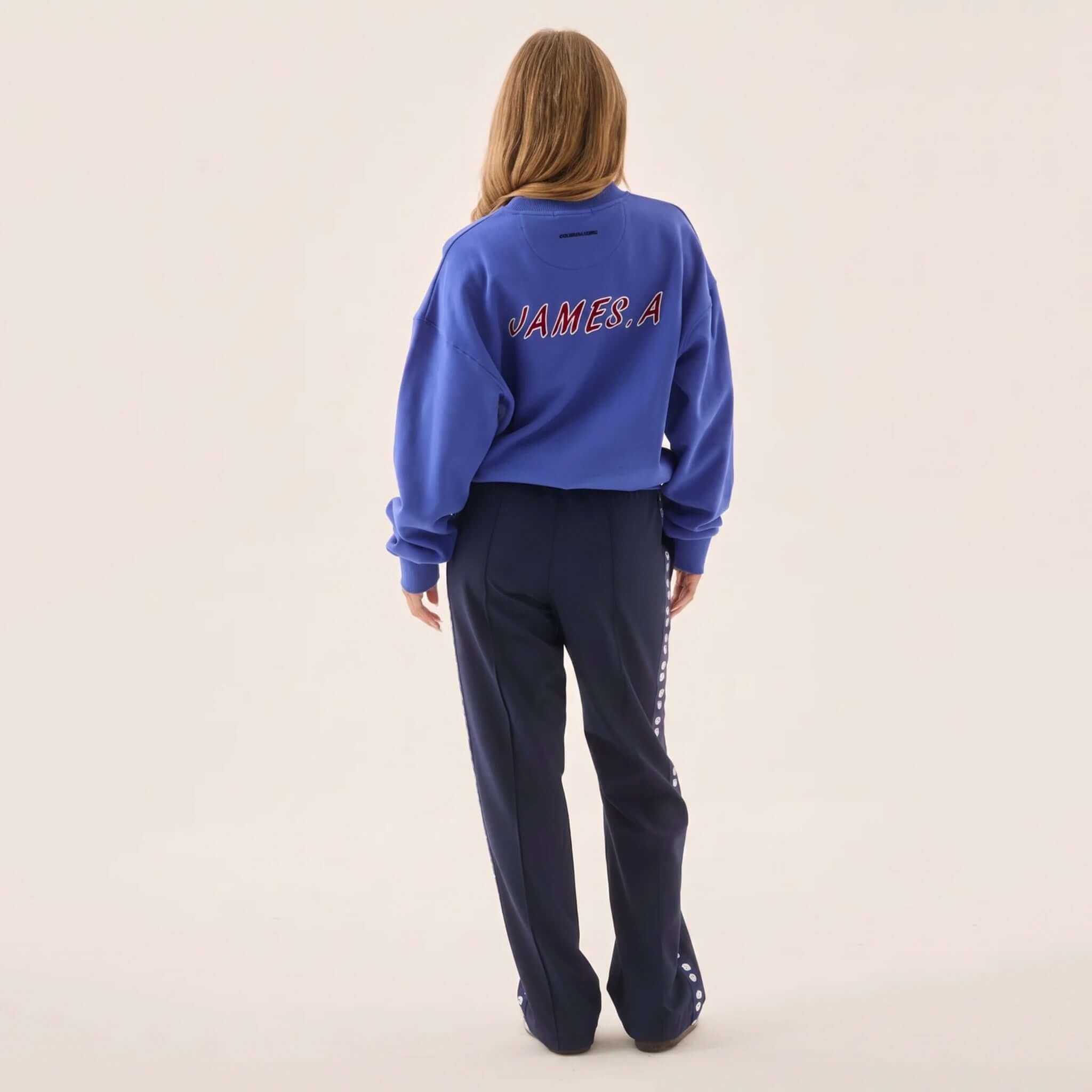 Araminta James Pomodoro Twill Pants - Midnight Navy worn with a blue JAMES.A sweatshirt from behind.