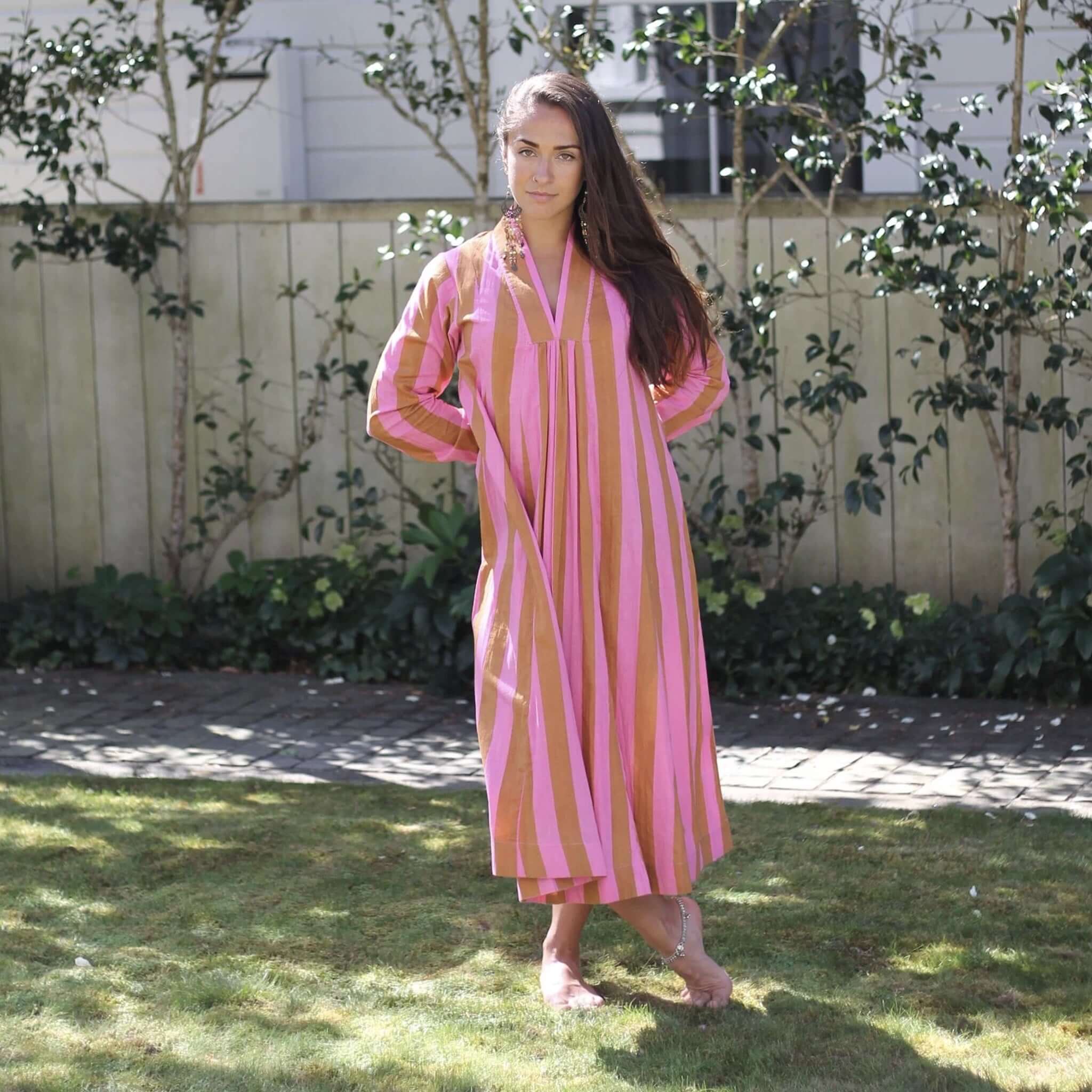 Art In My Wardrobe Diana Dress - Pink worn by a model in a garden, showcasing its vibrant pink and caramel stripes.