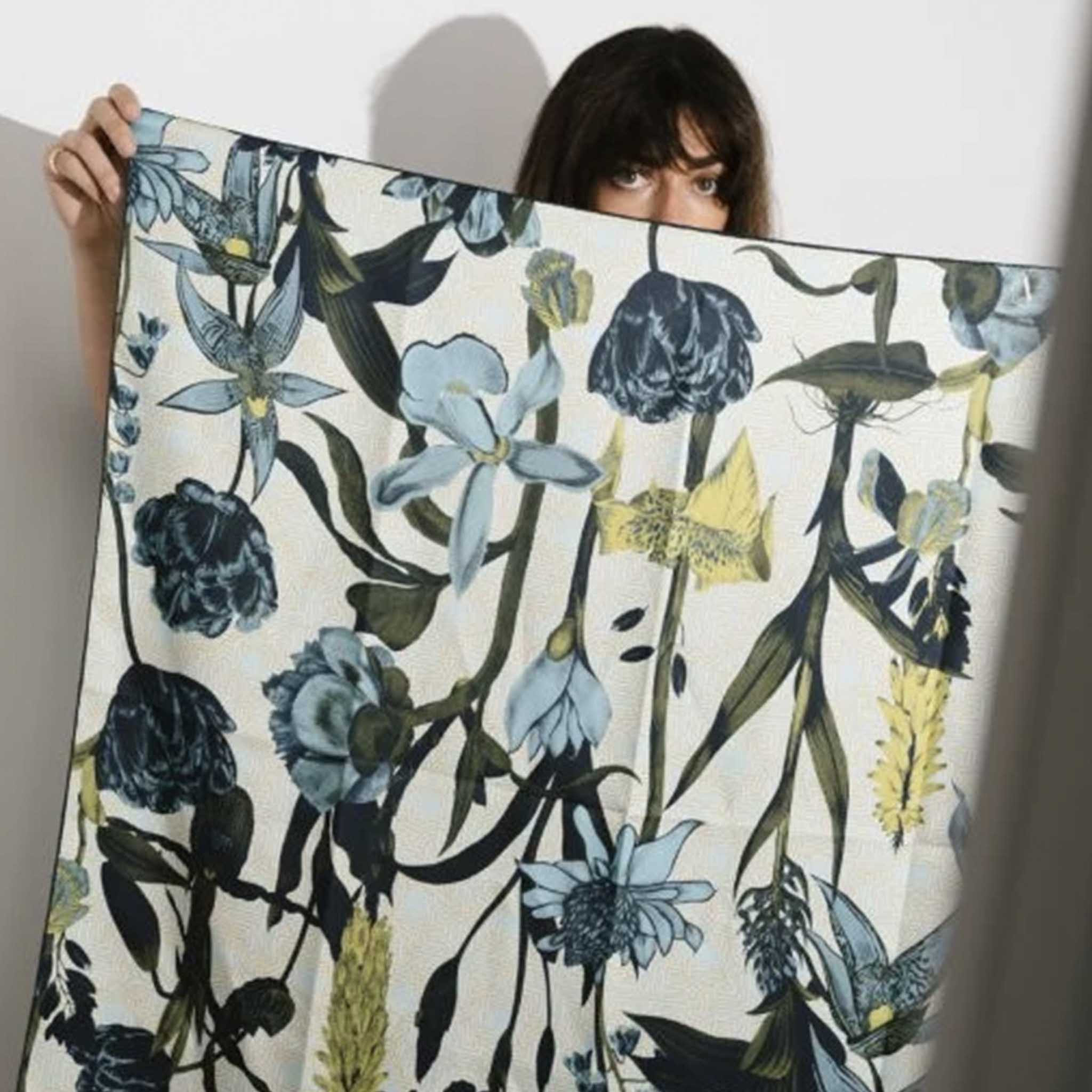 Alt Tag: Artifact Square Silk Scarf - Eos with blue and yellow botanical print on cream geometric background, held up by model