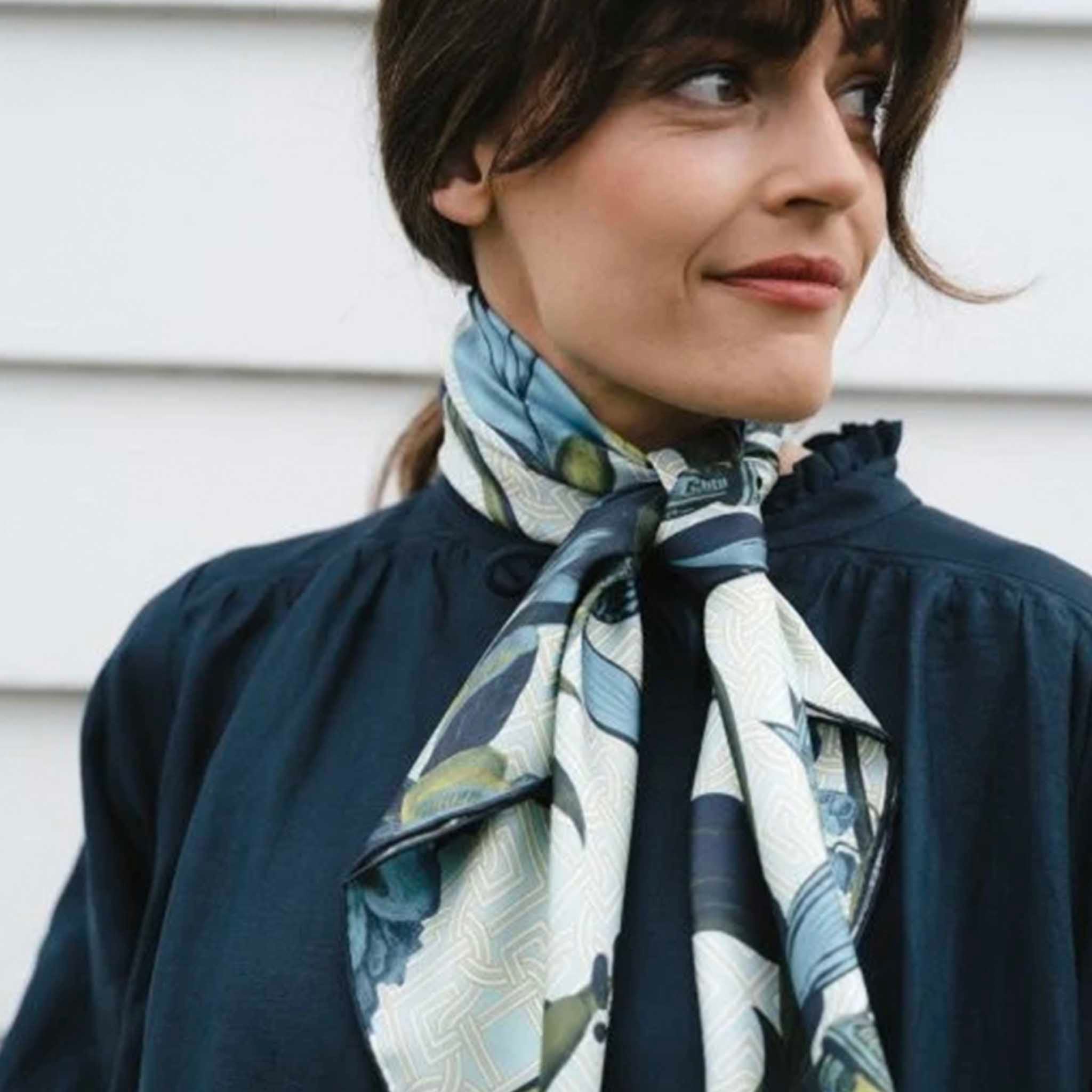 Alt Tag: Model wearing Artifact Square Silk Scarf - Eos in soft blue and yellow botanical print, tied around neck on cream geometric background