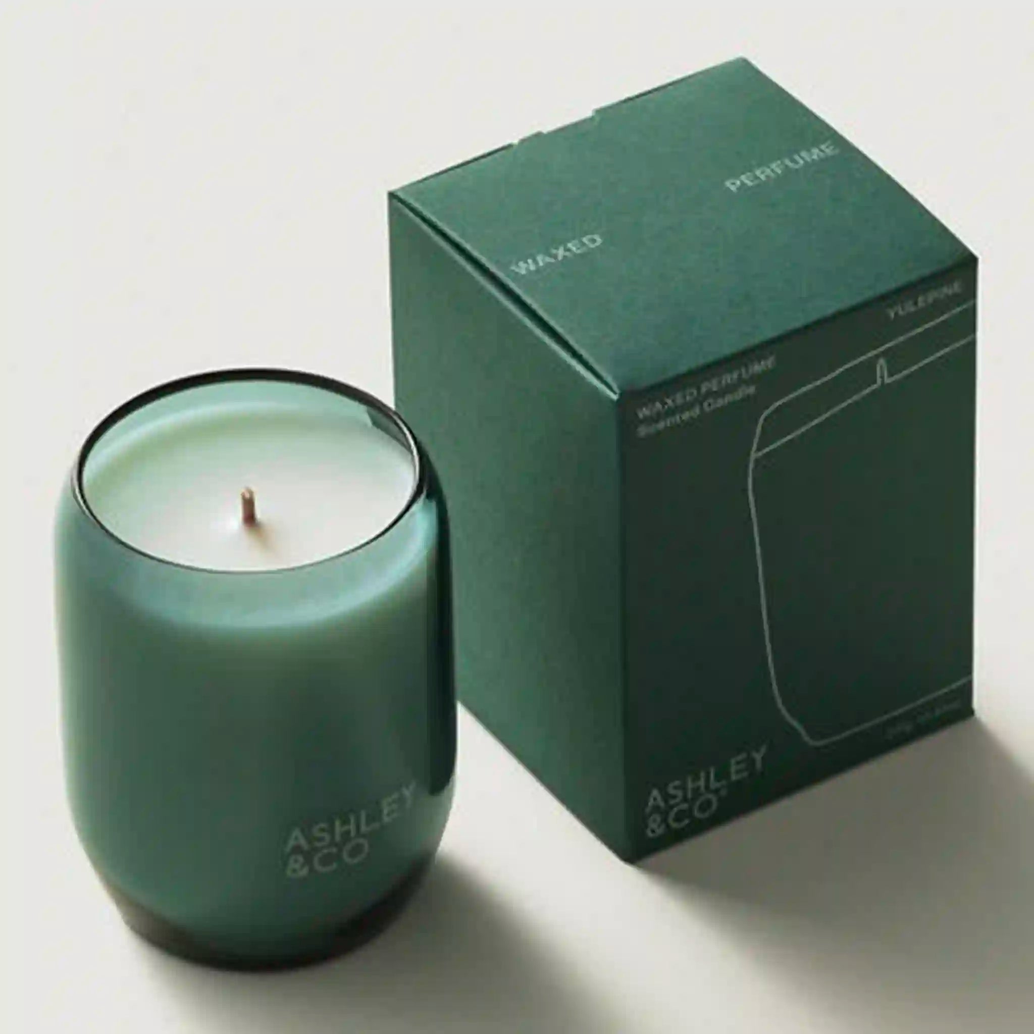 Green candle with 'Ashley & Co.' branding next to its packaging on a light background