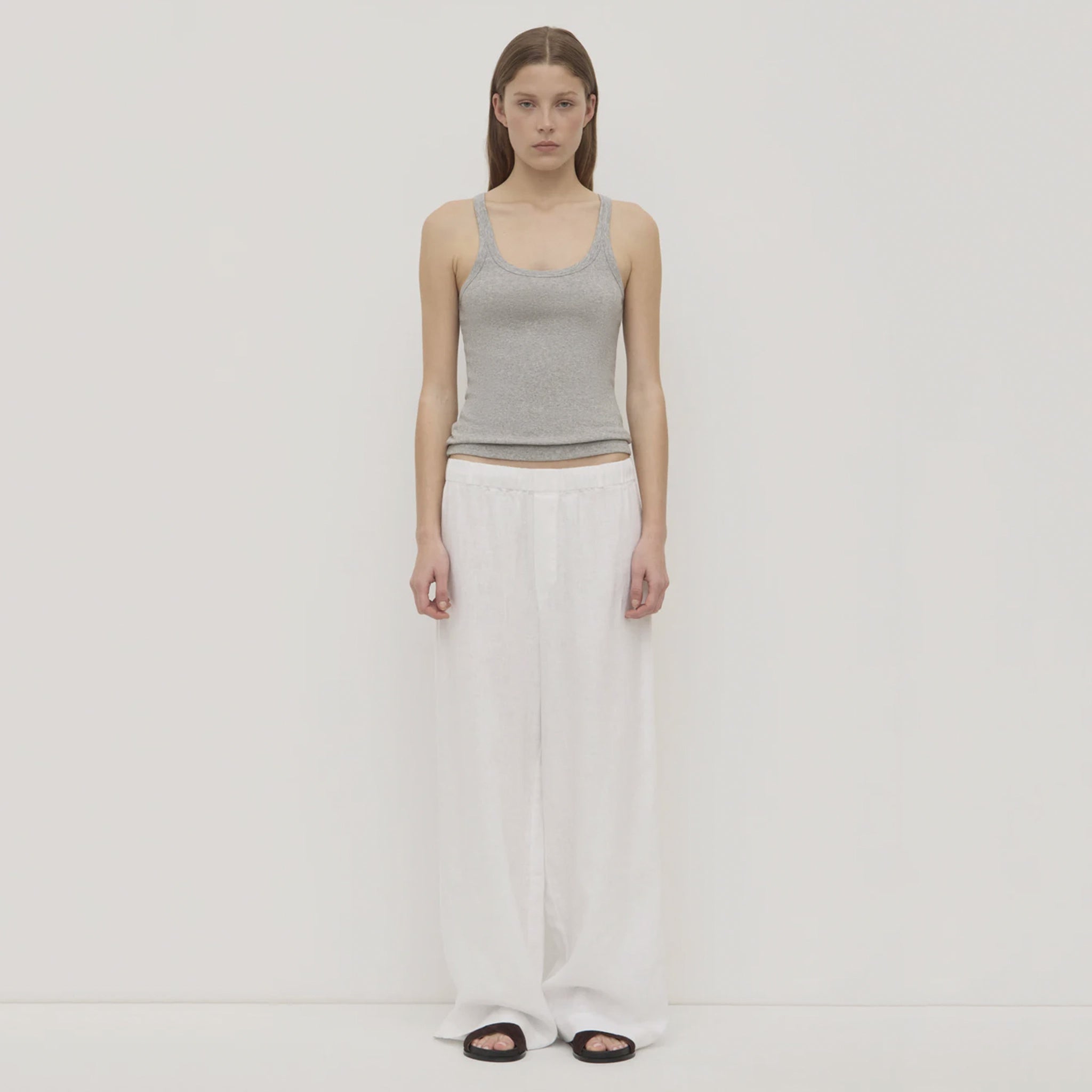 Woman wearing a gray tank top and white pants on a plain background