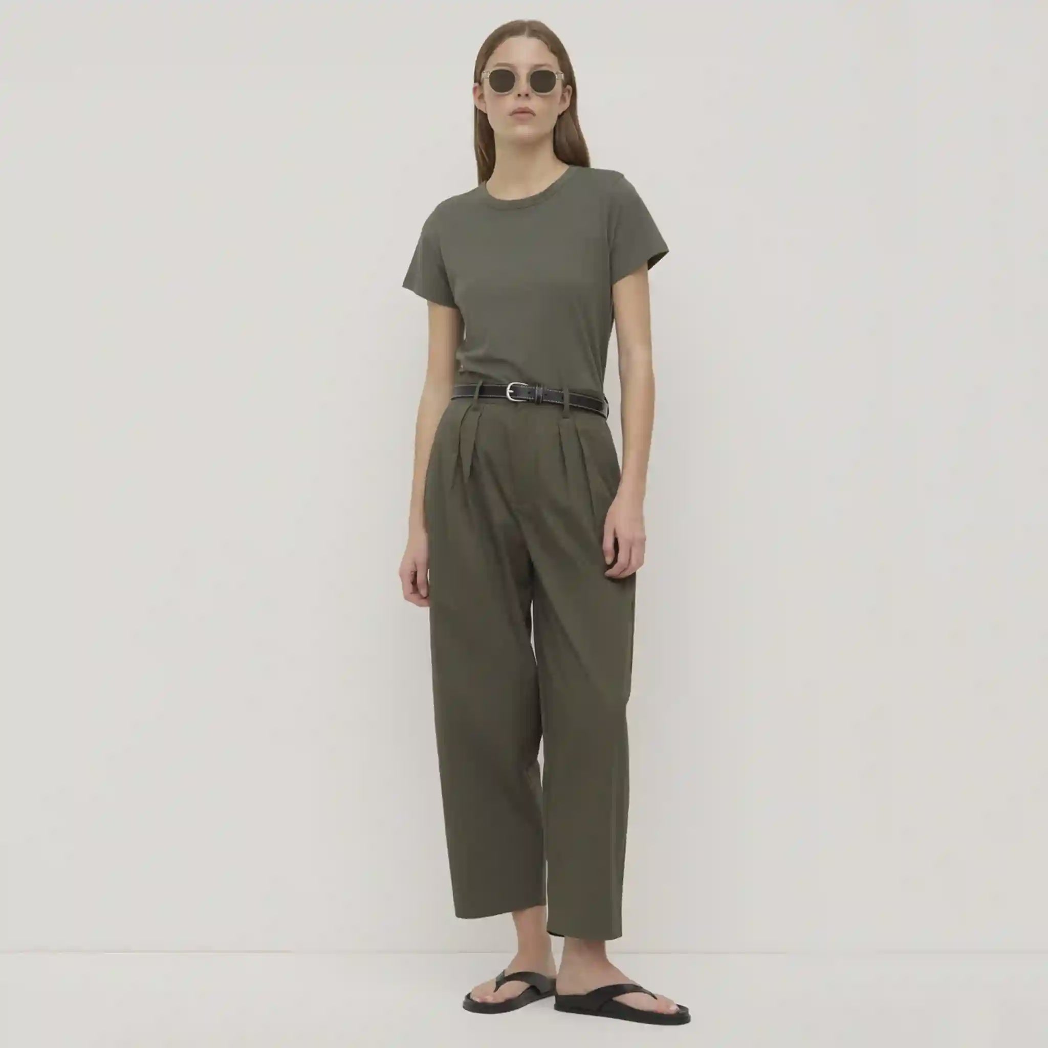 Woman wearing a green outfit with sunglasses on a plain background
